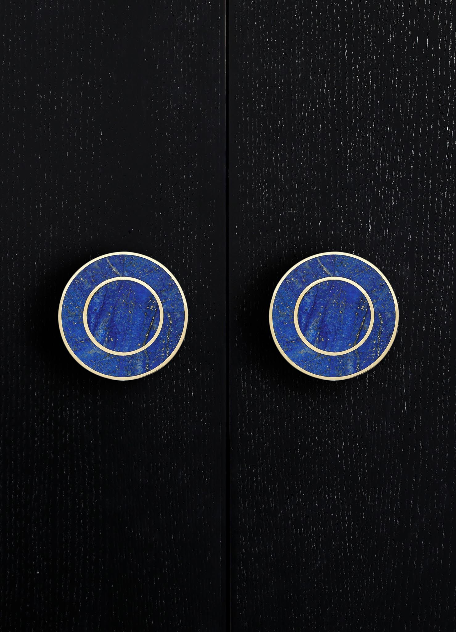 Round ceramic drawer pulls with a vivid blue glaze and gold speckled pattern, framed by white borders, mounted on a black textured surface.