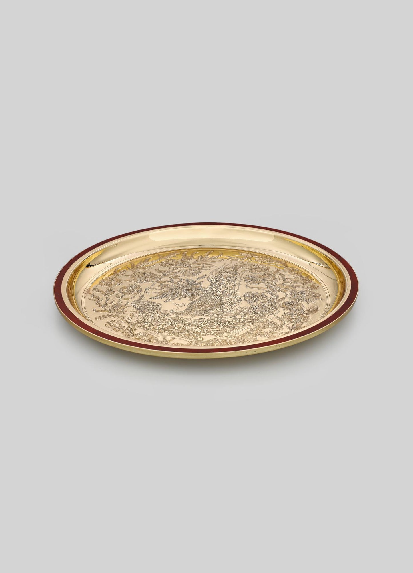 Decorative round tray made of metal with a gold finish, featuring intricate engraved motifs of a phoenix surrounded by floral and foliage patterns, with a dark red border.