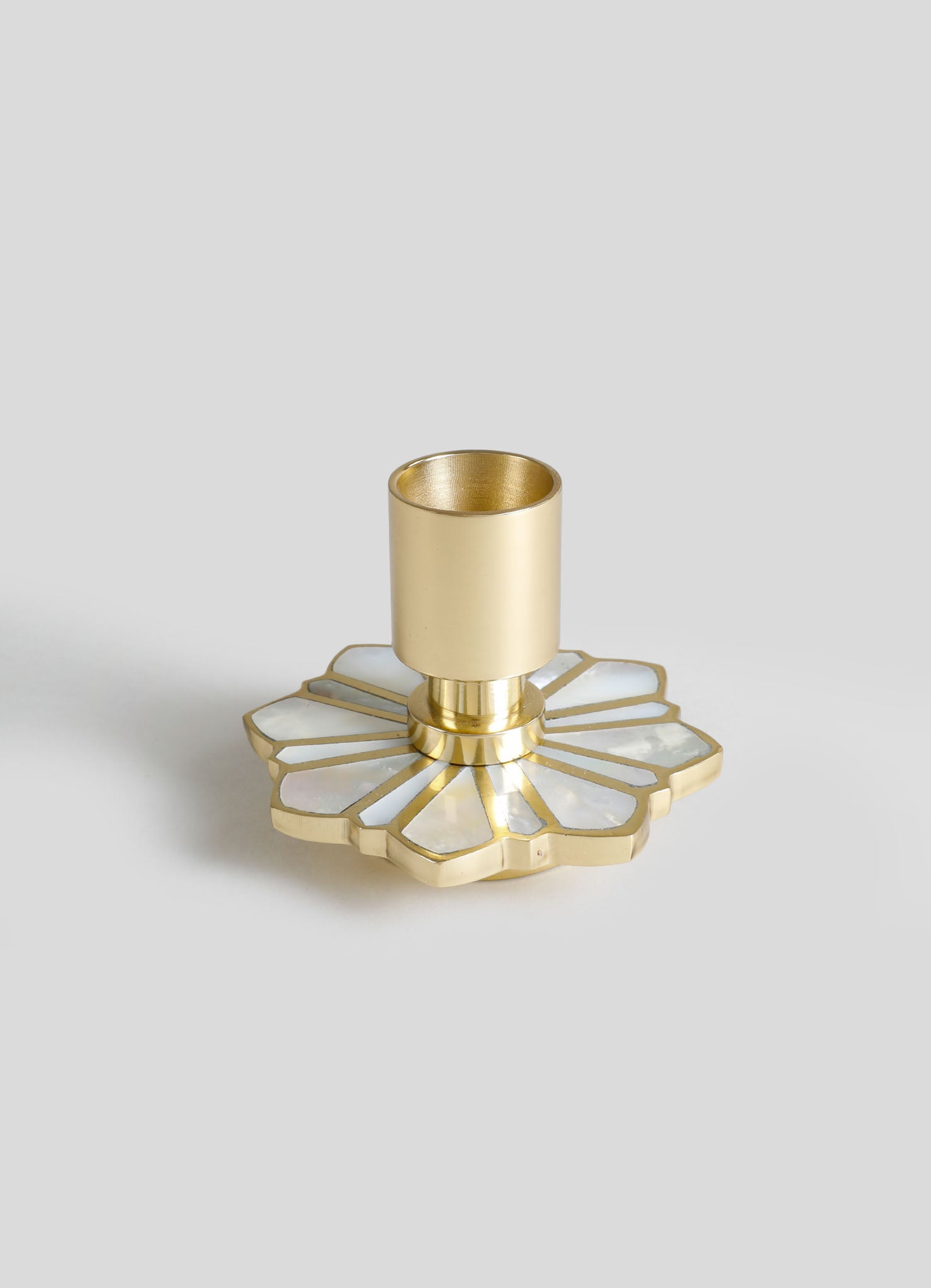 A gold candle holder with a cylindrical holder set on a decorative base featuring white mother-of-pearl inlay and a floral motif.