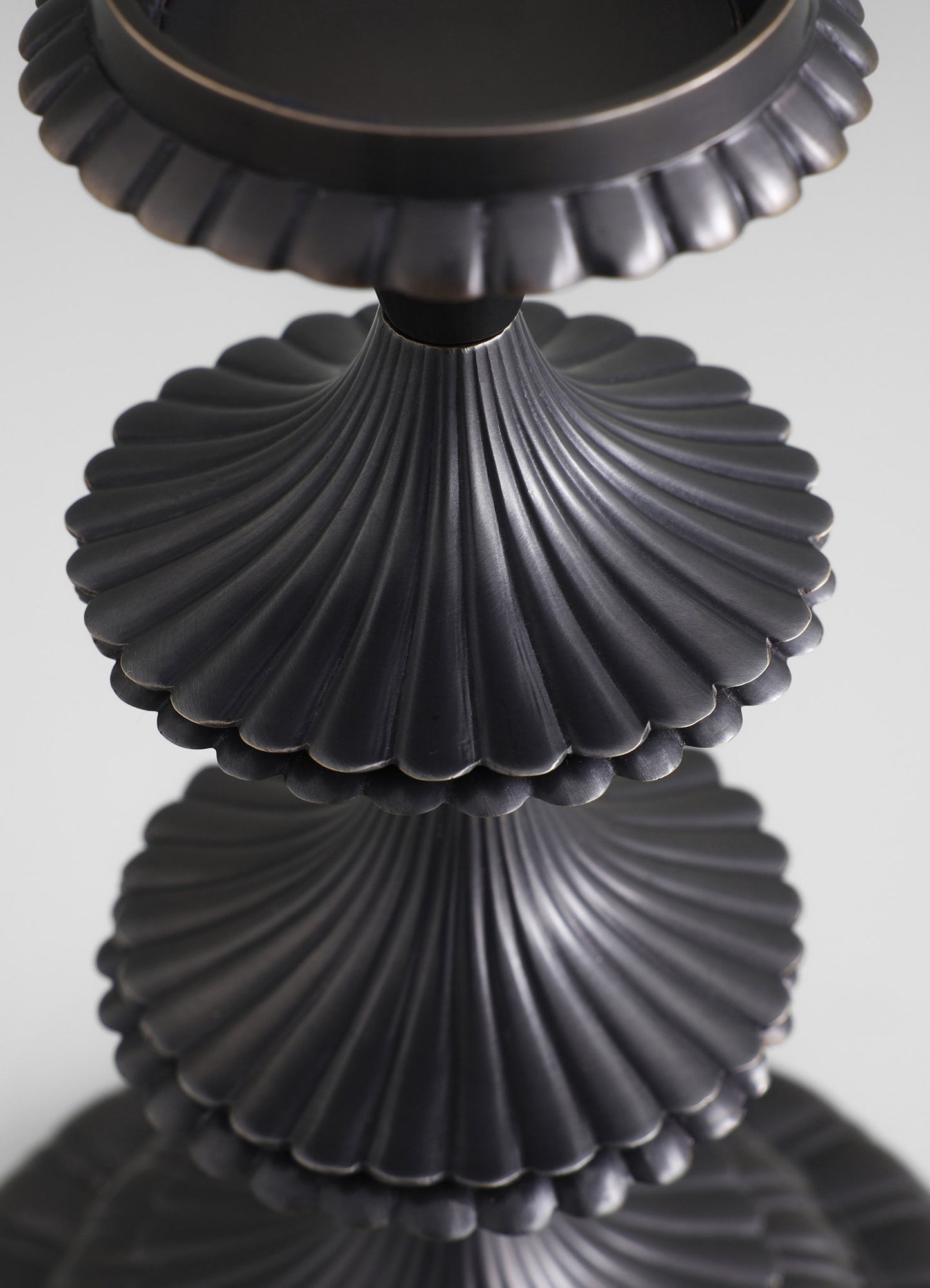 Black ceramic candle holder with a scalloped edge and fluted, fan-shaped design, featuring a matte finish and a reflective surface below.