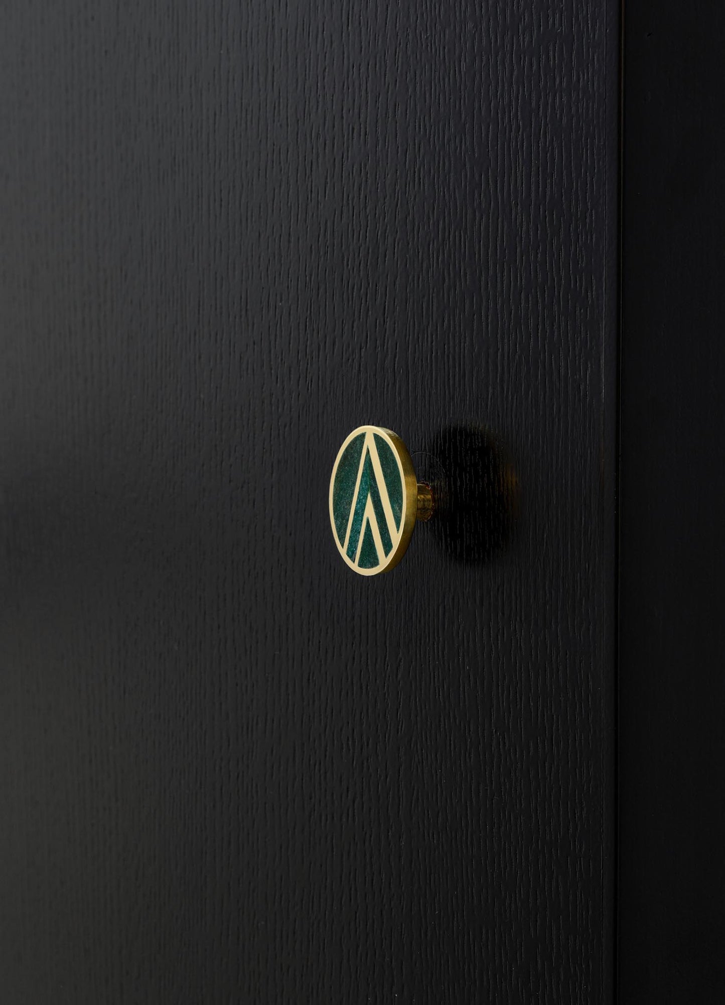 A close-up of a black textured wooden surface with a small oval-shaped metal knob featuring a green and white geometric pattern and a gold border.