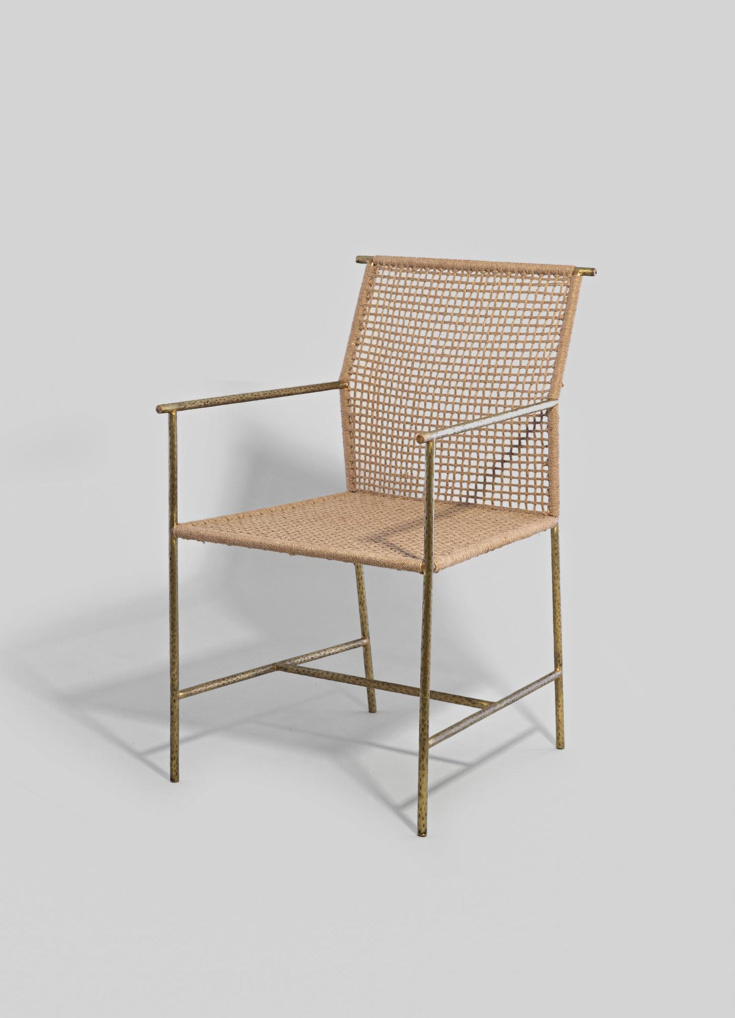 A modern lounge chair with a brass frame and a woven rattan backrest and seat, featuring a minimalist design with clean lines and a neutral beige color.