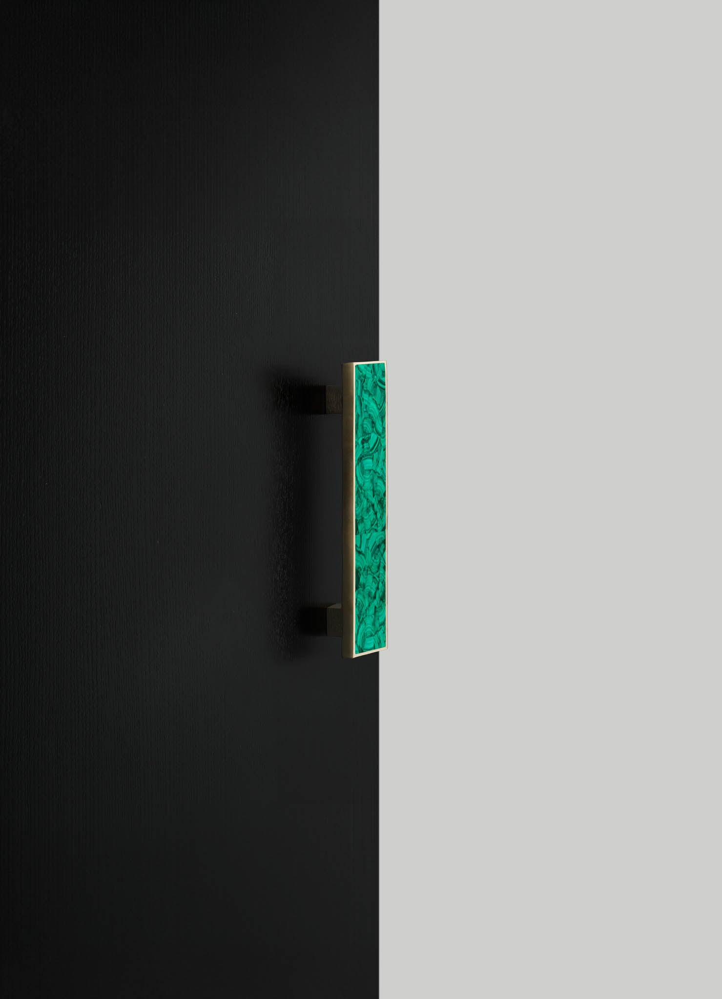 A rectangular wall sconce with a green marbled glass panel and a brass frame mounted on a black wall. The design has a contemporary style with a focus on metallic and vibrant color contrast.