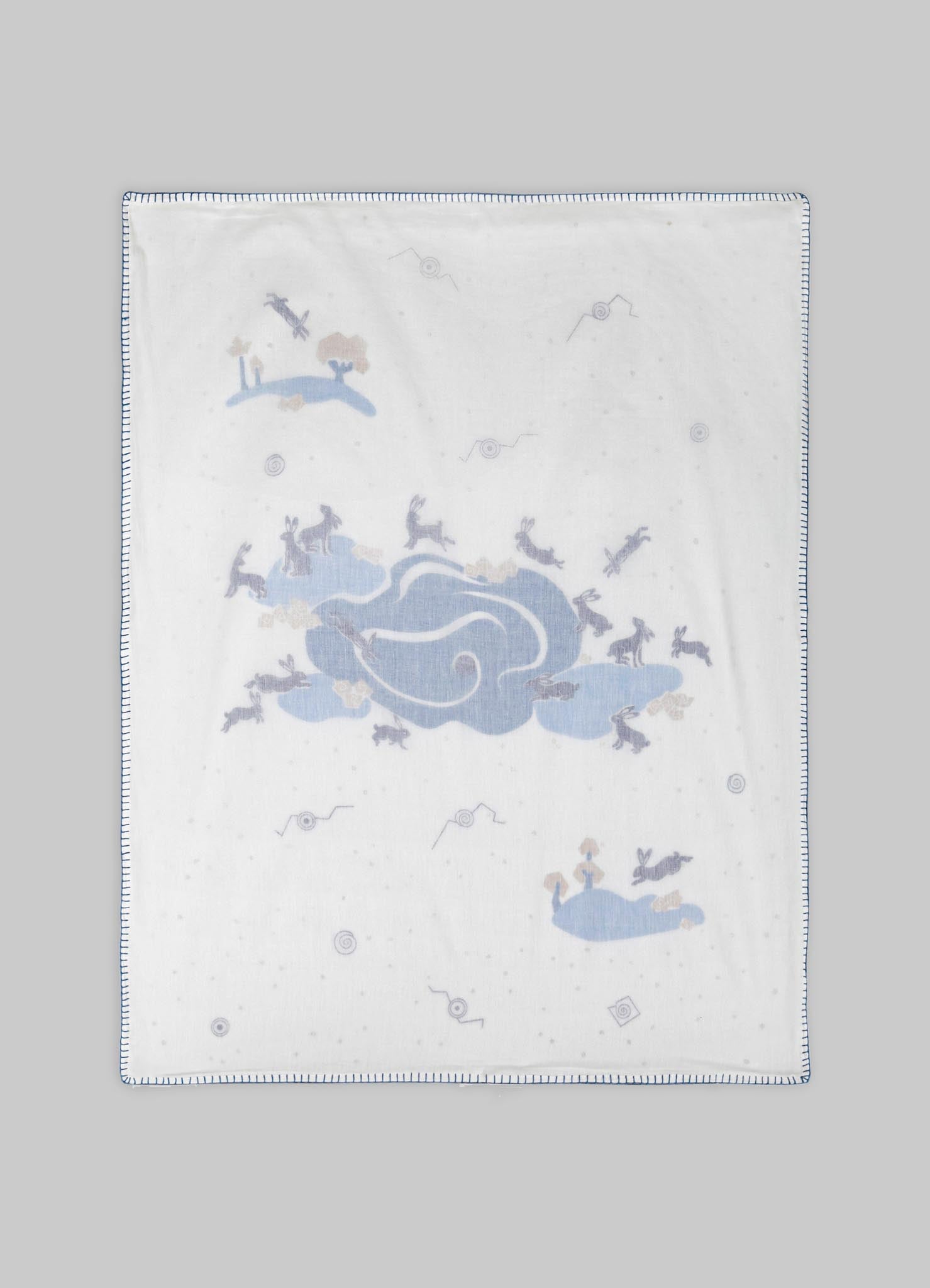 Cotton blanket featuring embroidered bunny motifs in pastel blue and beige, with a stitched border detail in dark blue.