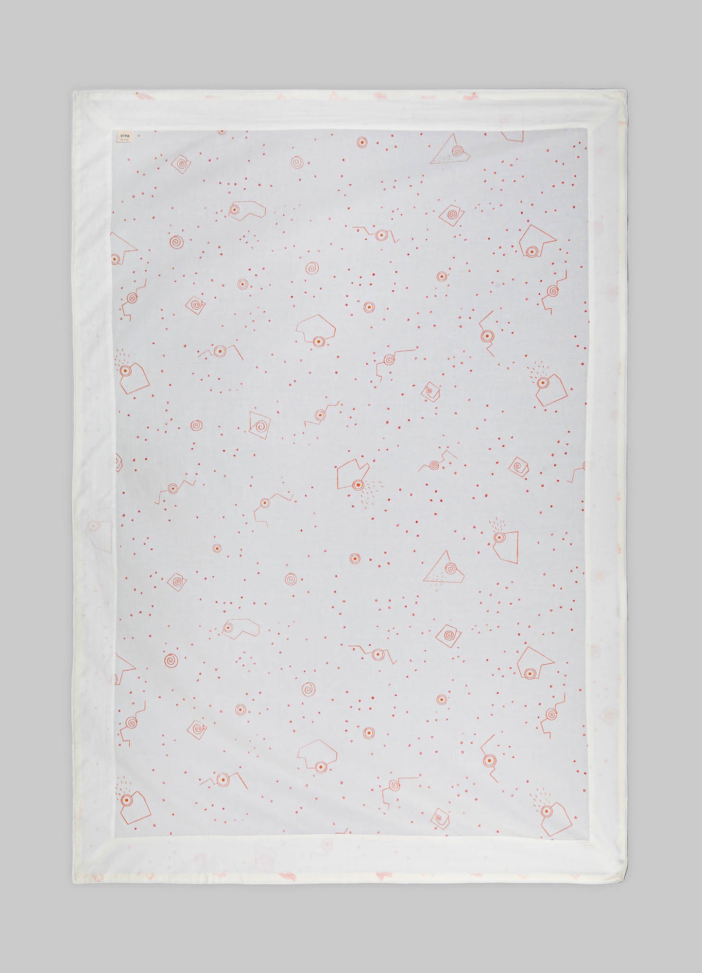 Printed table runner made of white fabric with red geometric and dotted motifs, framed by a simple border.