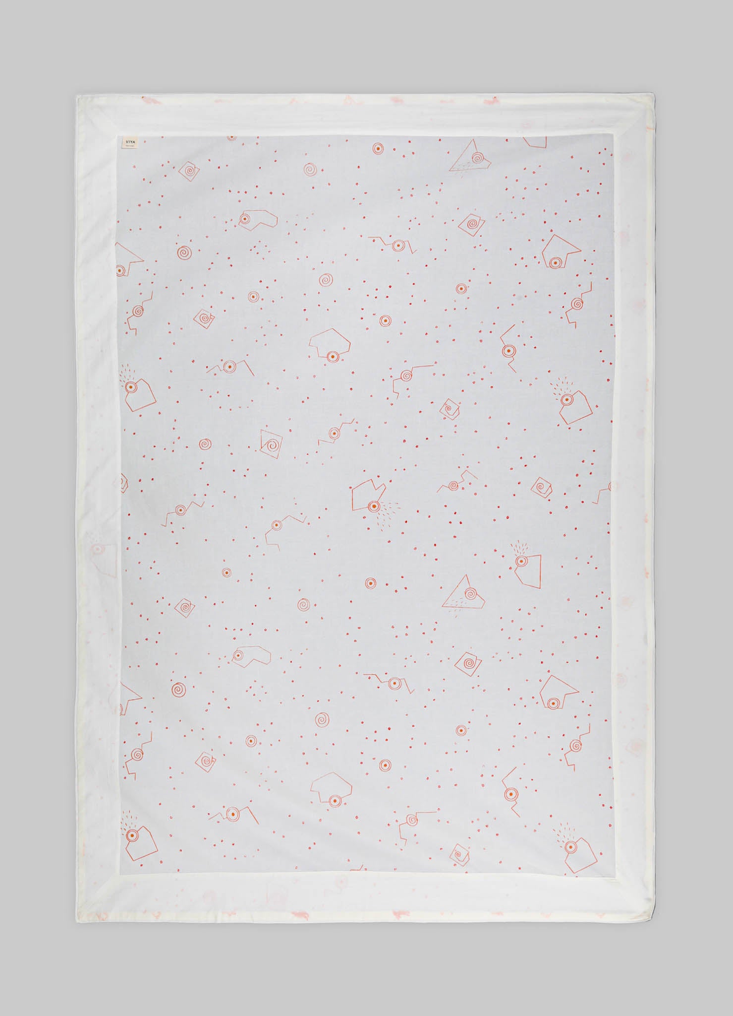 Printed table runner made of white fabric with red geometric and dotted motifs, framed by a simple border.