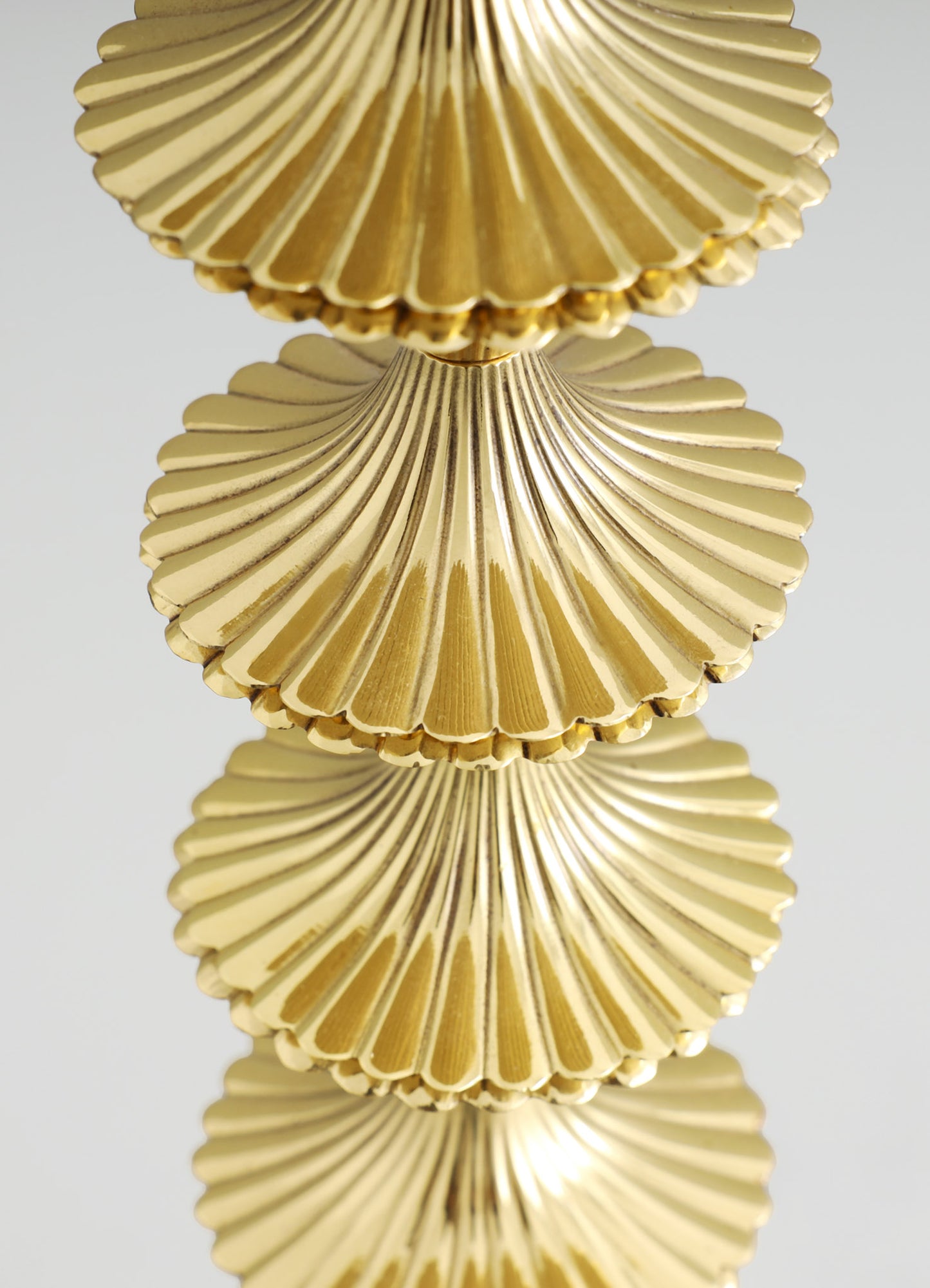 Gold-colored metal table decoration or sculpture featuring overlapping, ribbed, fan-shaped elements with a shiny finish and scalloped edges. The design has a contemporary and luxurious style with a reflective, polished surface.