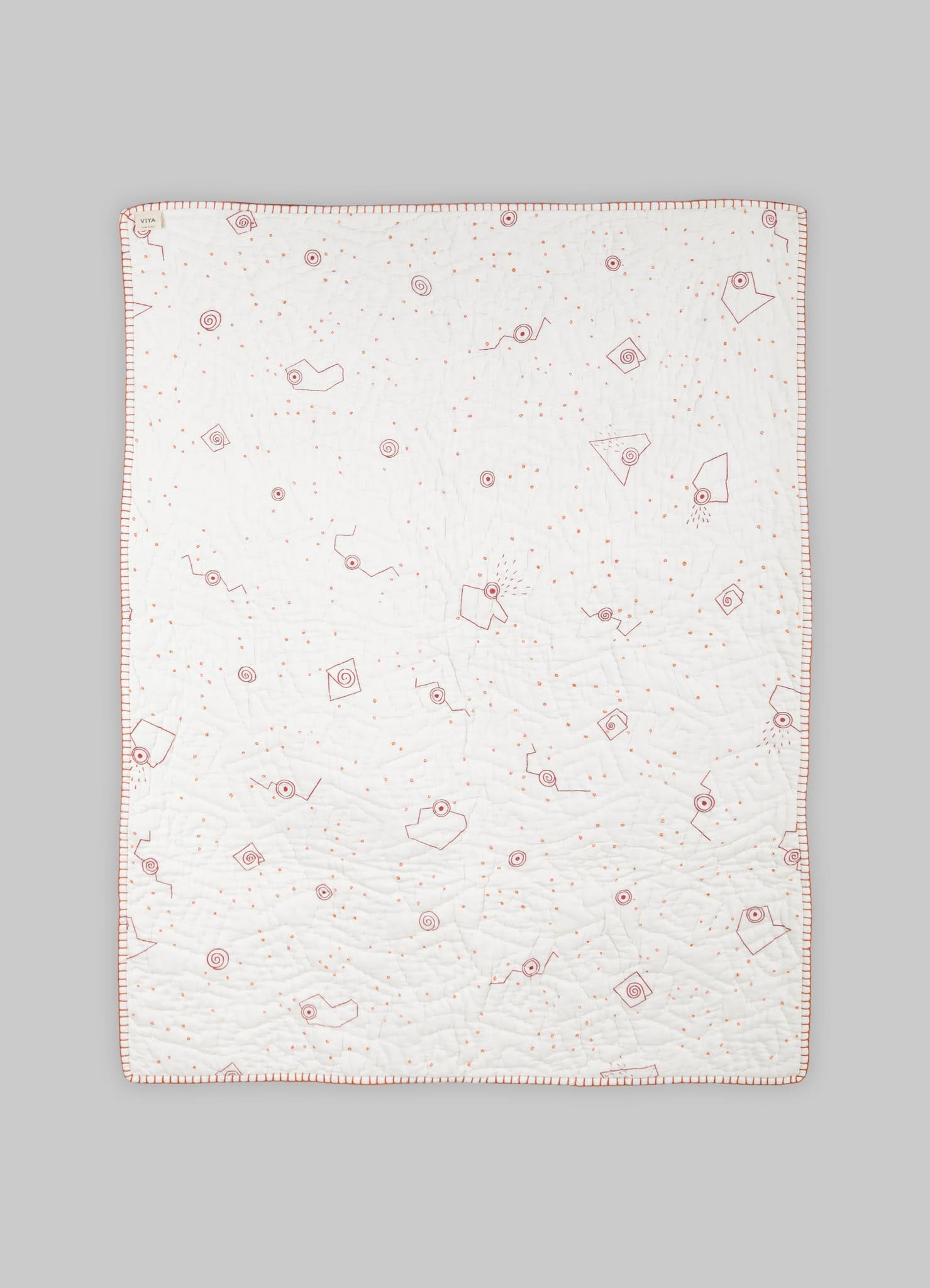 Cotton quilt with embroidered geometric motifs and a subtle color palette, edged with a contrasting border.