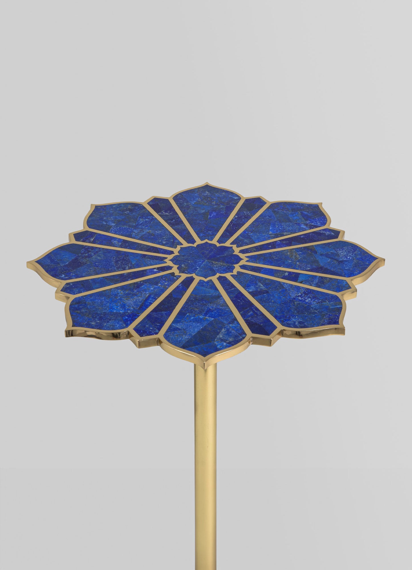 A round side table with a blue marble top featuring a floral pattern divided by gold accents, supported by a slim gold metal stem. The table has a contemporary style with a luxurious and decorative appearance.