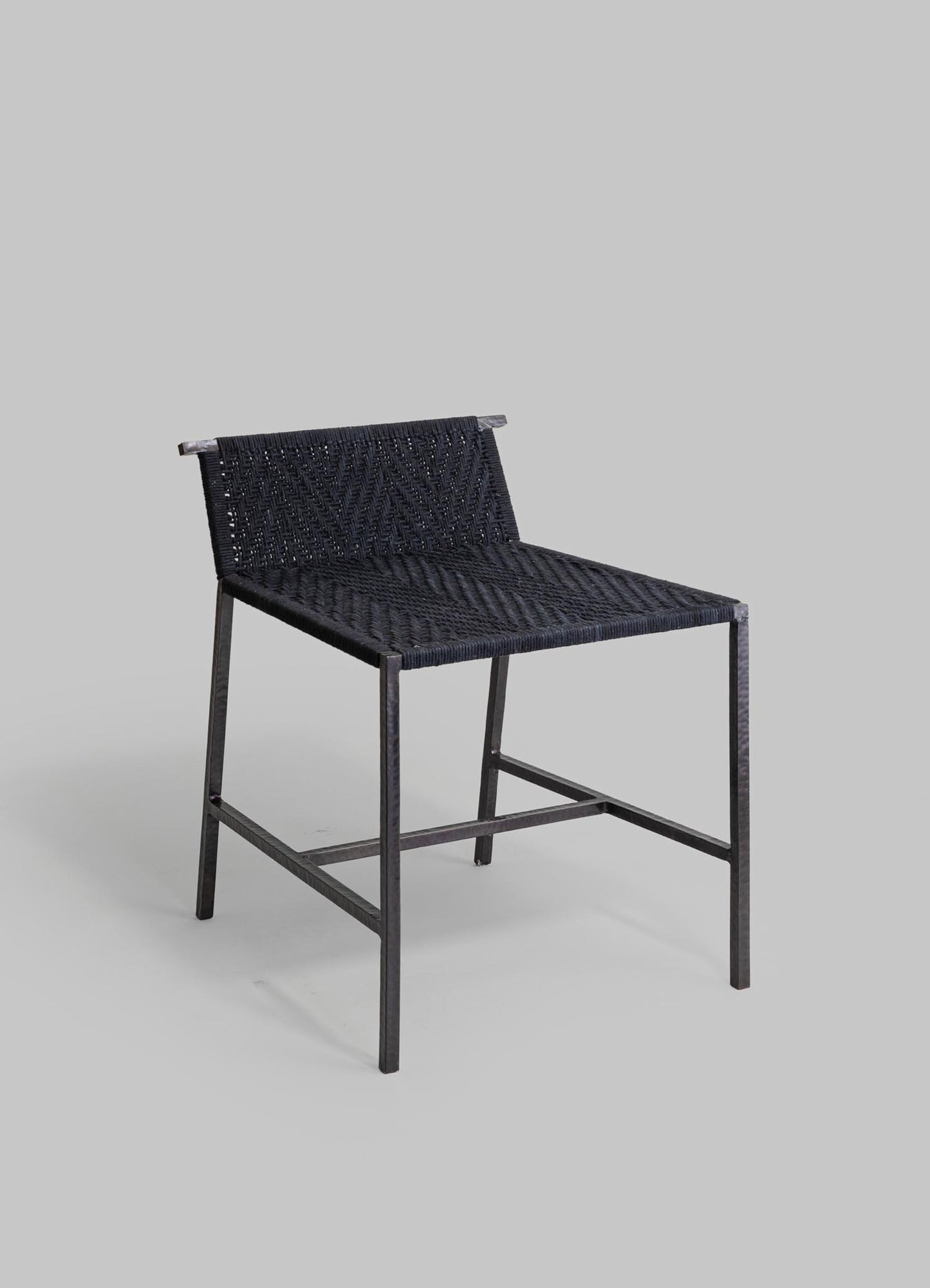A black woven chair with a metal frame, featuring a seat and backrest made of intricately patterned woven material, set against a plain gray background.