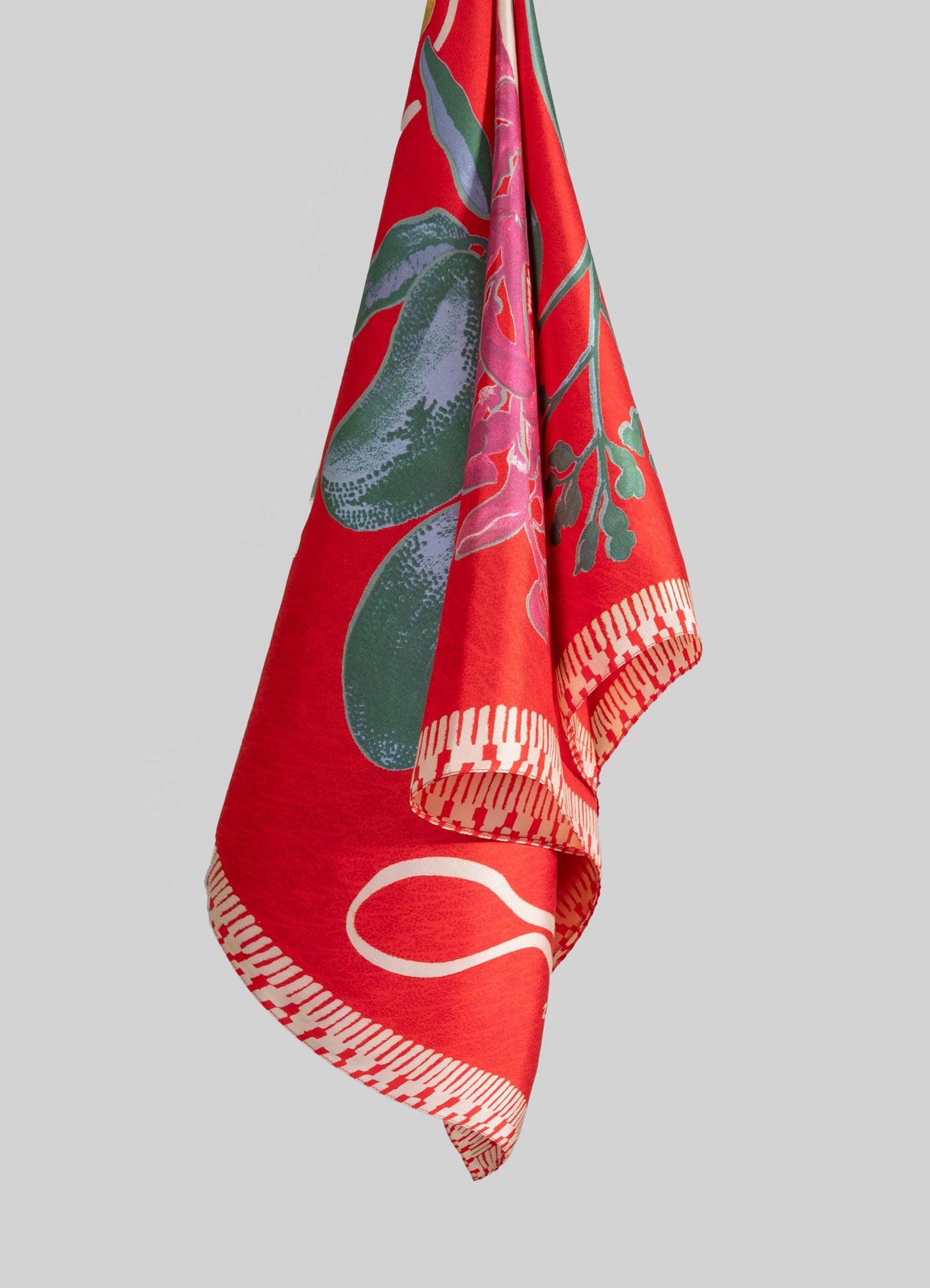 Colorful textile with bold red background, floral and botanical motifs in shades of green, pink, and purple, featuring a decorative border with a linear pattern. The fabric appears to be a lightweight cloth, suitable for wrapping or accenting home decor or fashion items.