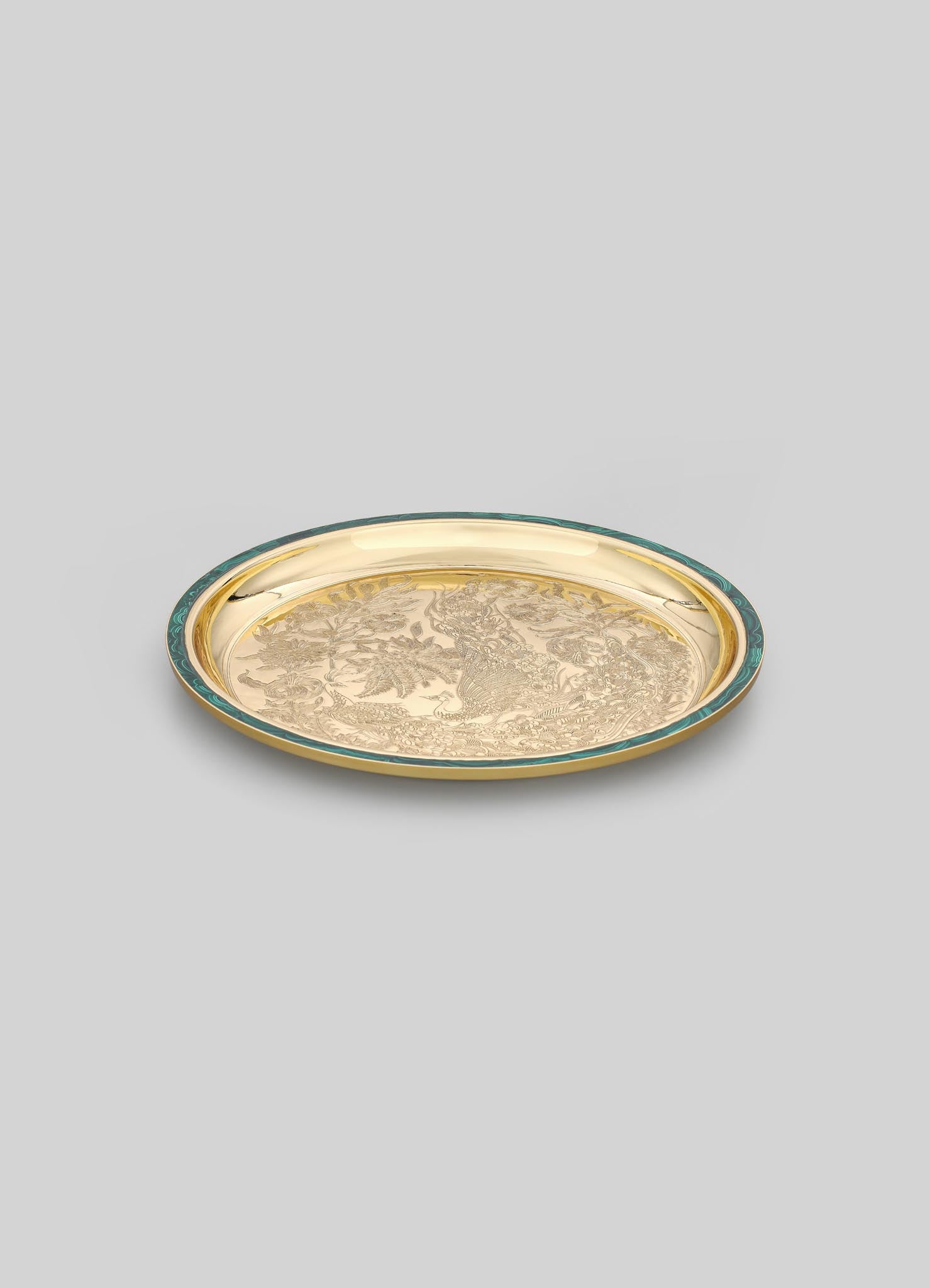 A round decorative tray with a gold-tone finish and engraved intricate motifs, bordered by a teal-colored rim.