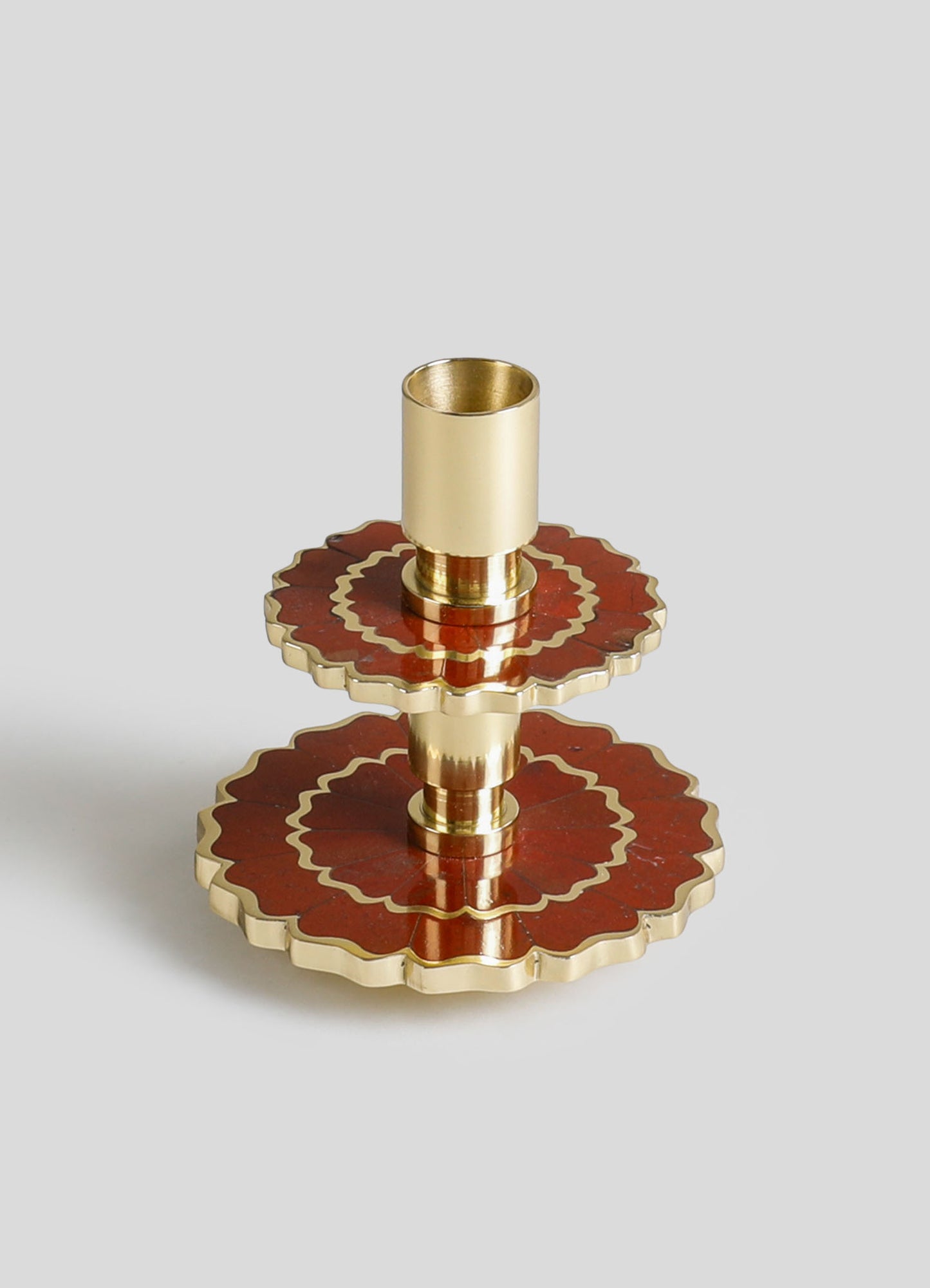 A decorative candle holder with a brass finish and layered circular base featuring red and gold patterns, blending metallic and bold colors with an ornate, handcrafted style.