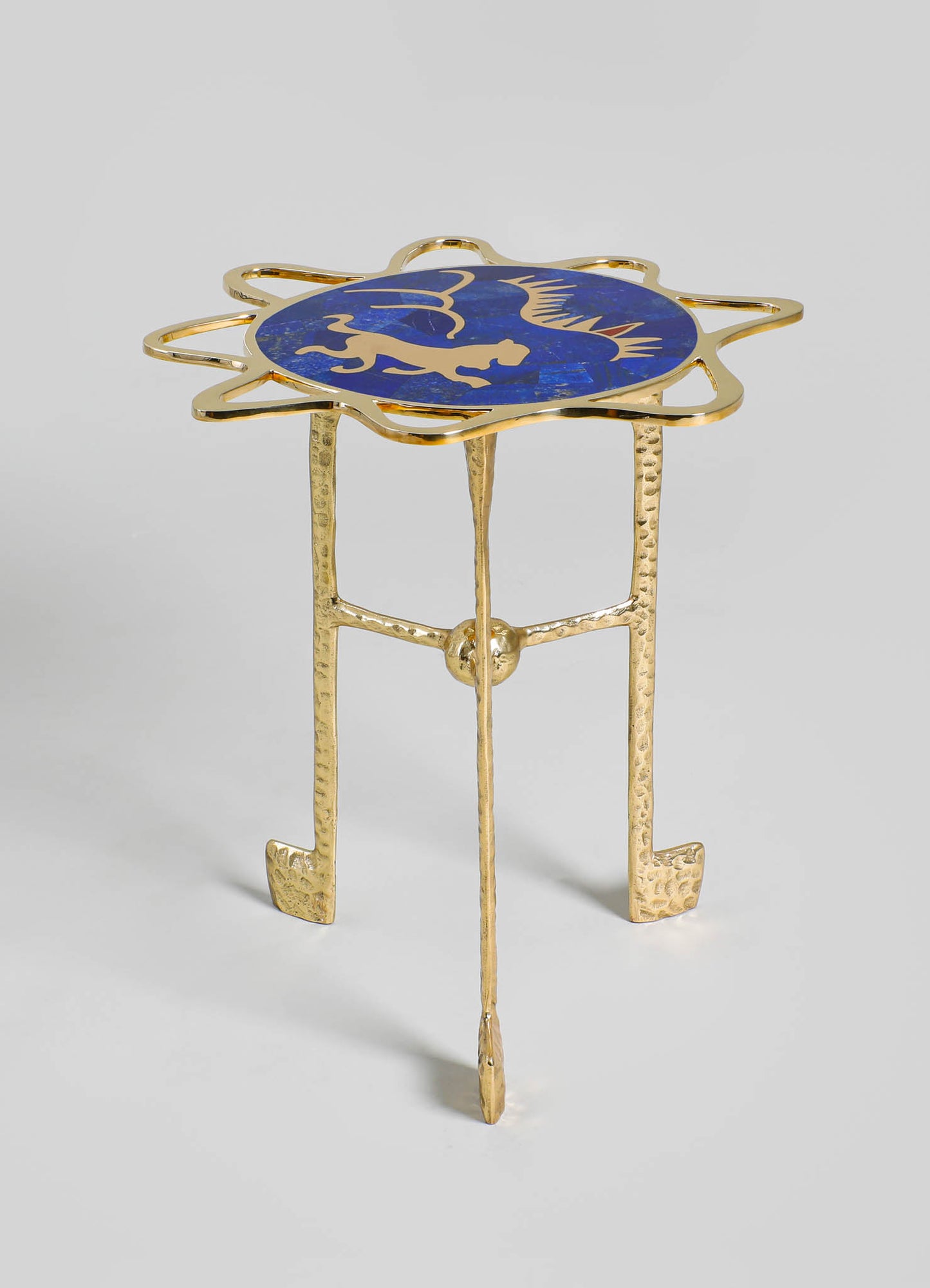 Glass and brass side table with a circular blue and gold motif top featuring an abstract design, supported by textured brass legs with a hammered finish.