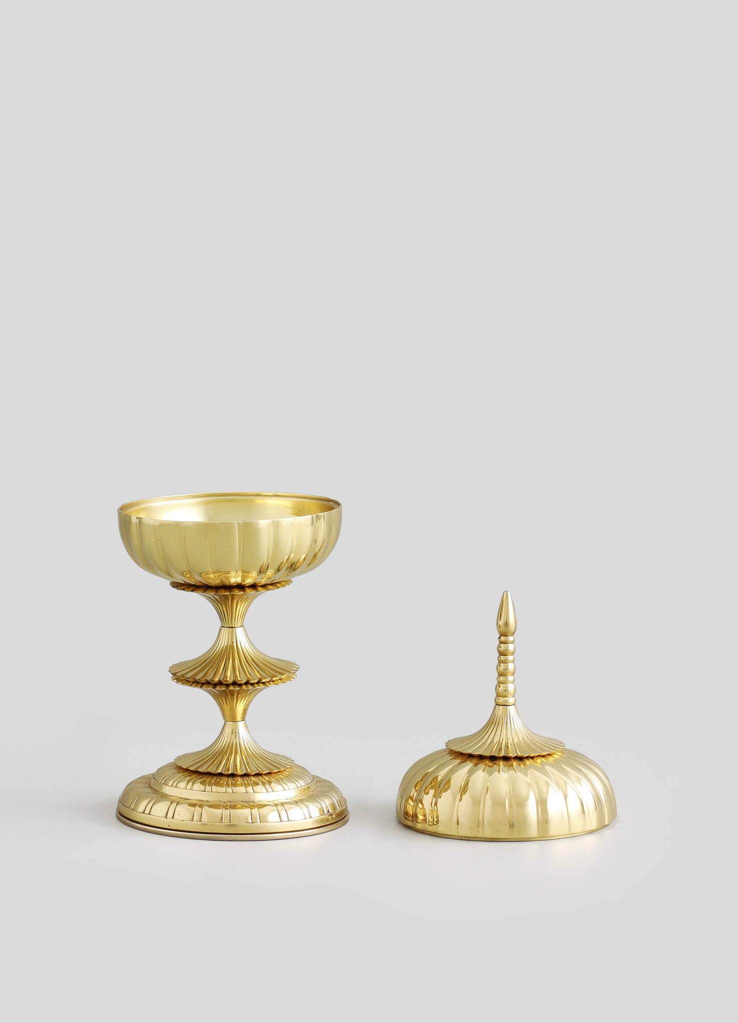 Brass decorative objects with a ribbed, scalloped pattern, featuring a reflective gold finish and elegant, sculptural forms.