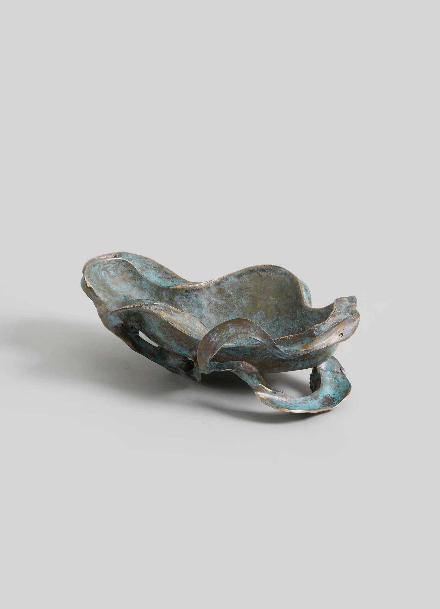 A decorative metal bowl with an organic, flowing shape and a patina finish in shades of blue and bronze, featuring a sculptural, handcrafted appearance.
