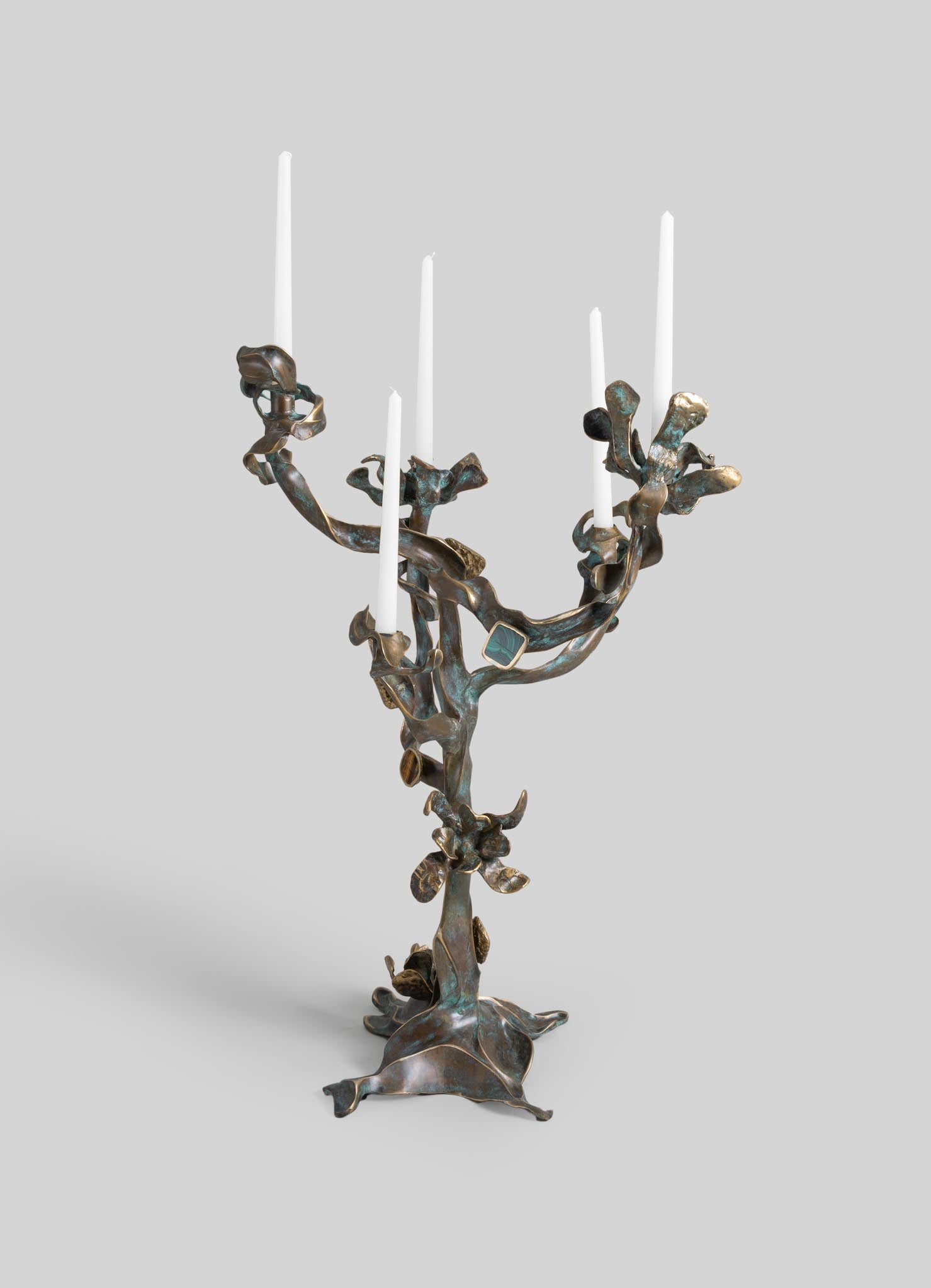 Bronze candelabrum with an organic, abstract design resembling flowing branches, holding five white taper candles. The piece has a rustic finish with hints of patina, evoking an artisanal and contemporary aesthetic.