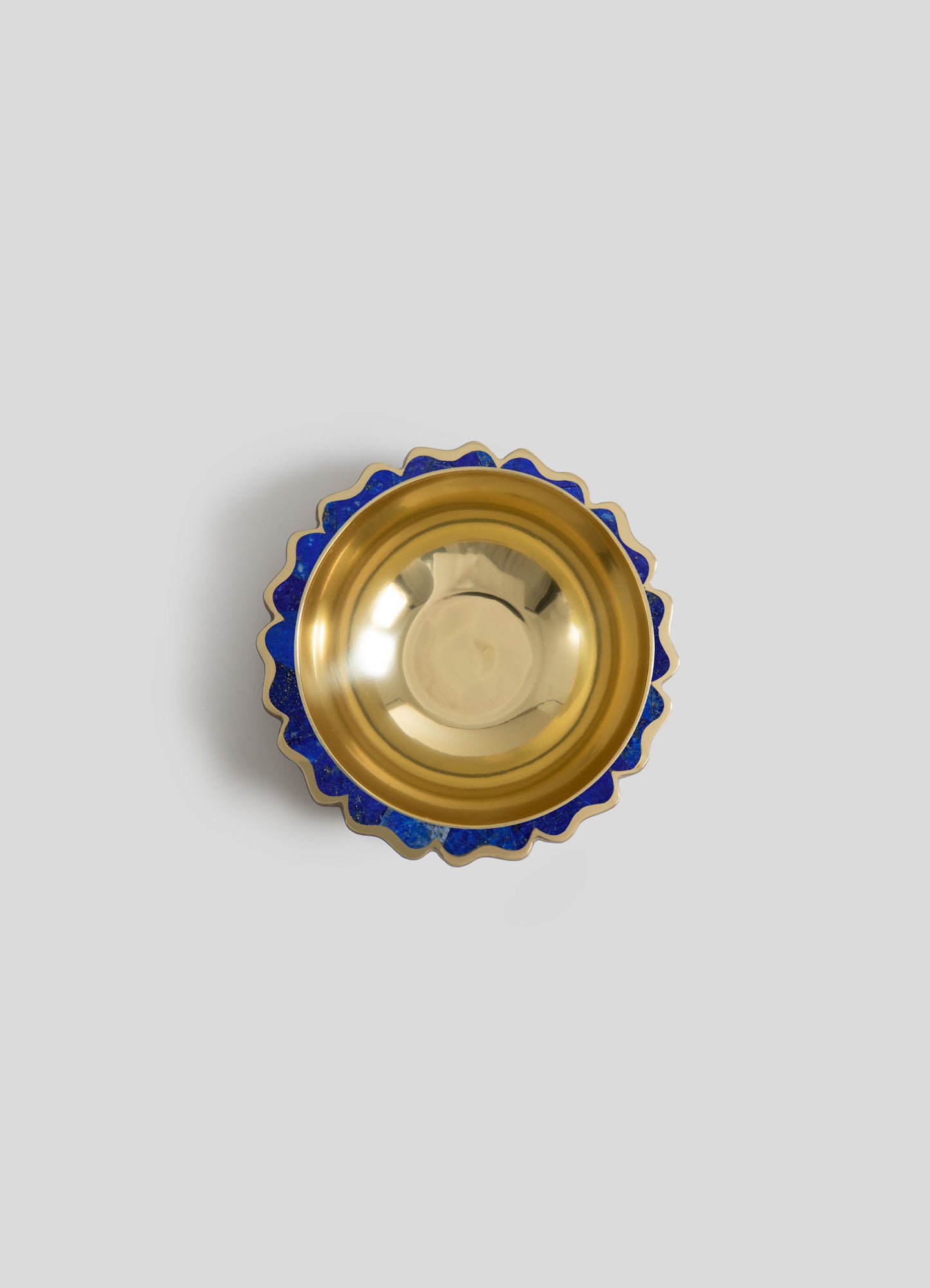 A decorative bowl with a gold metallic interior and a scalloped rim featuring a blue and gold pattern, set against a plain light gray background.