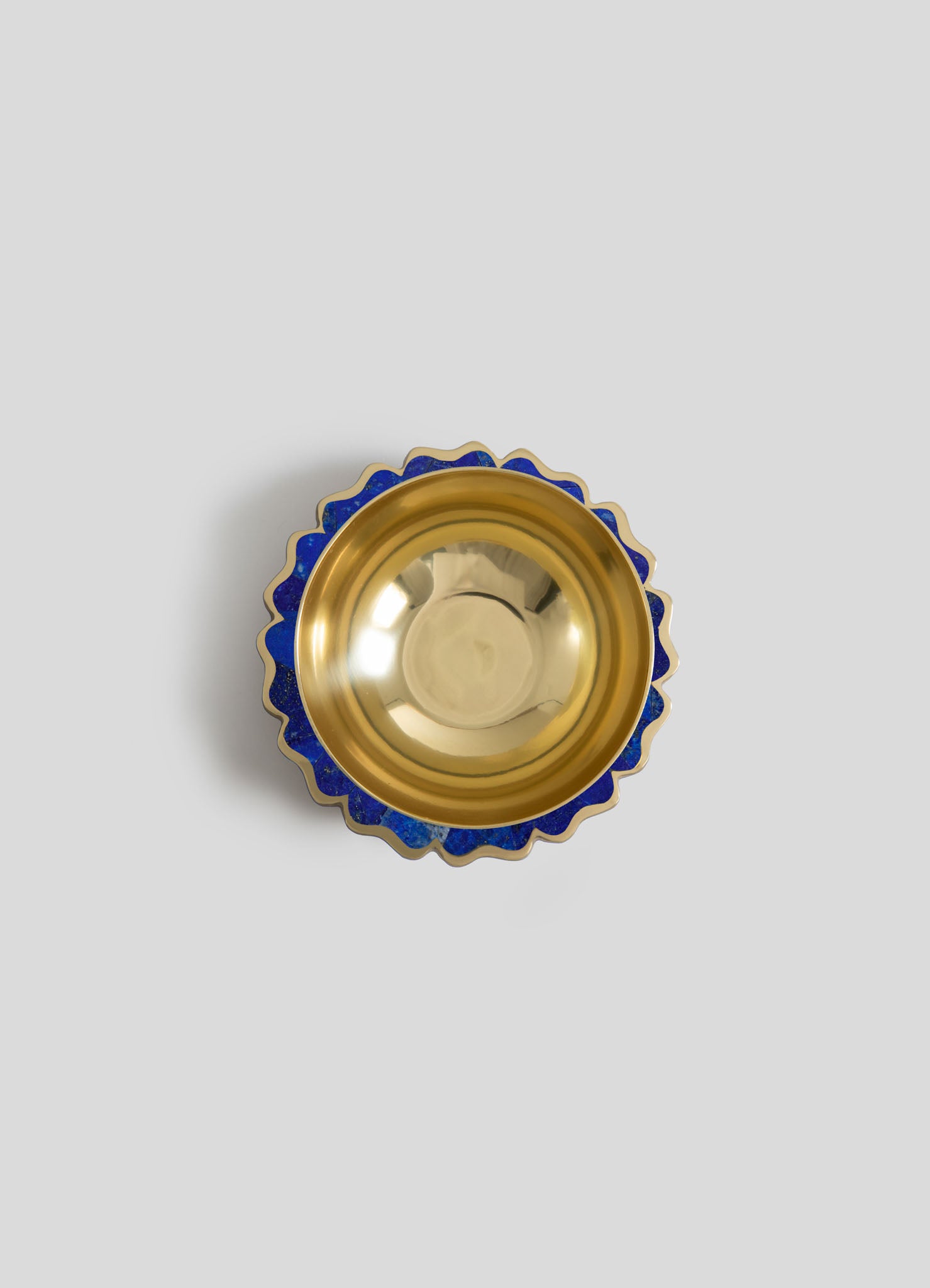 A decorative bowl with a gold metallic interior and a scalloped rim featuring a blue and gold pattern, set against a plain light gray background.
