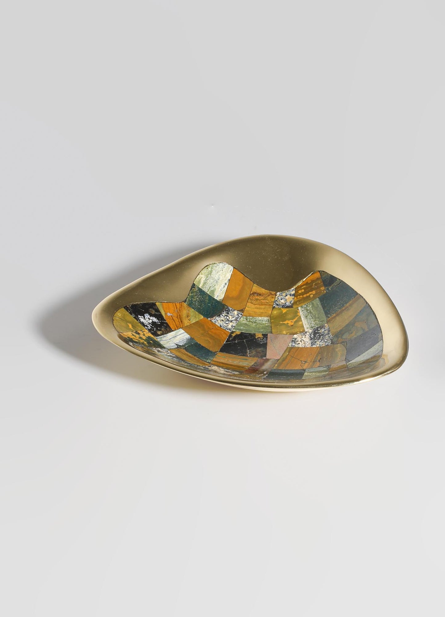 A decorative ceramic dish with an irregular oval shape, featuring a glossy beige exterior and an interior mosaic pattern of multicolored stones in shades of orange, green, black, and white.