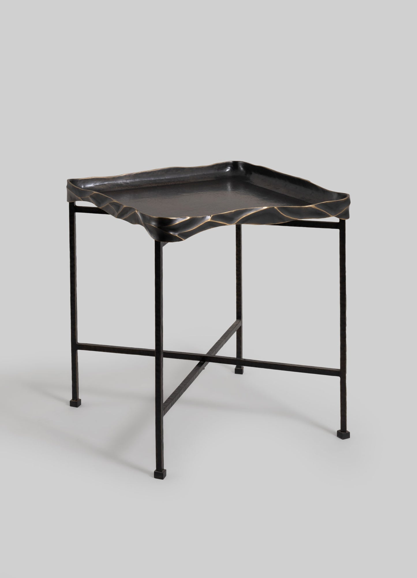 Black metal side table with a textured, wavy-edge tray top in matte finish and a minimalist frame, set against a plain light gray background.