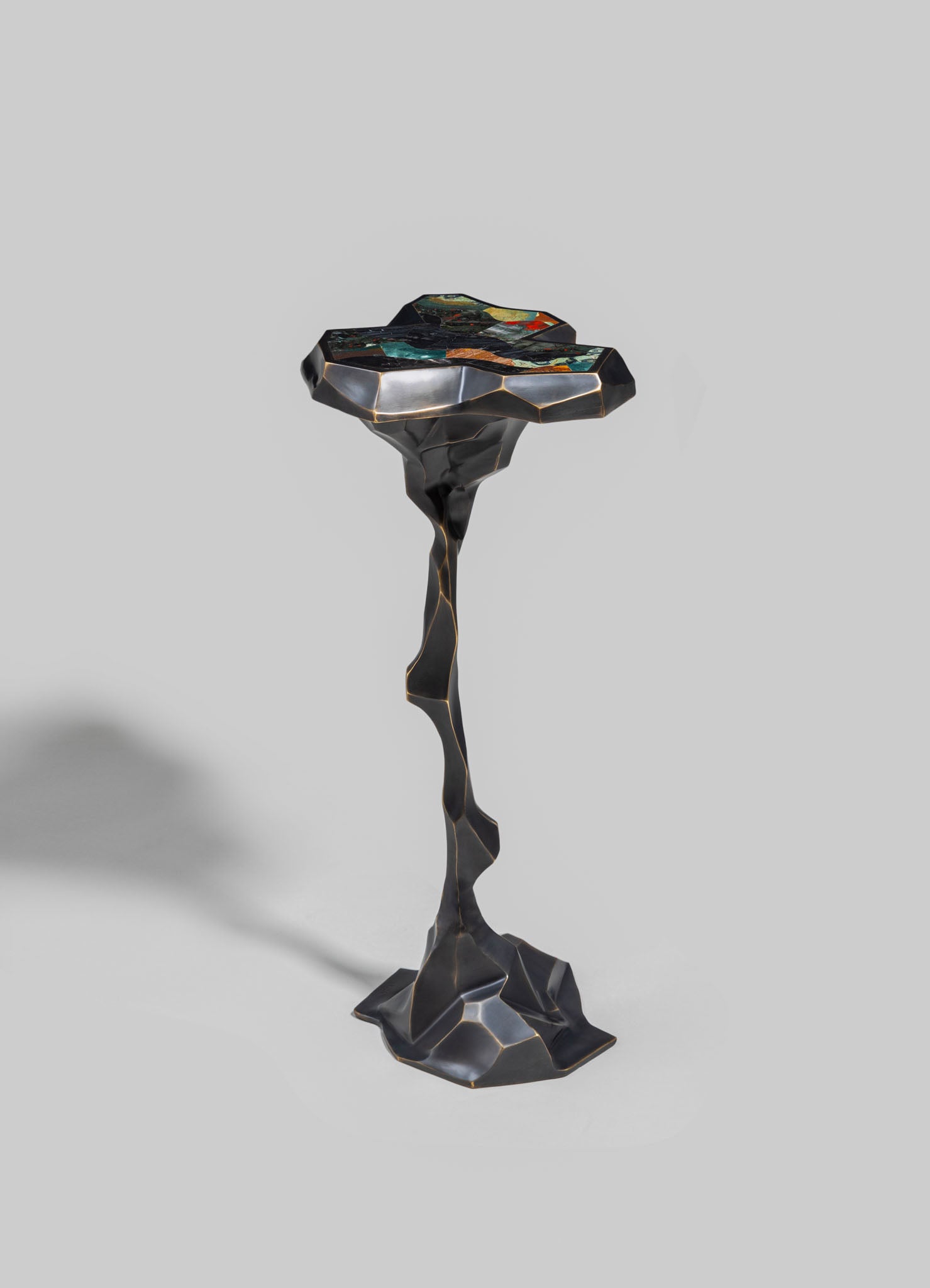 A sculptural side table with a twisted, organic-shaped base in black and gold accents, featuring a colorful mosaic top with geometric and abstract patterns.