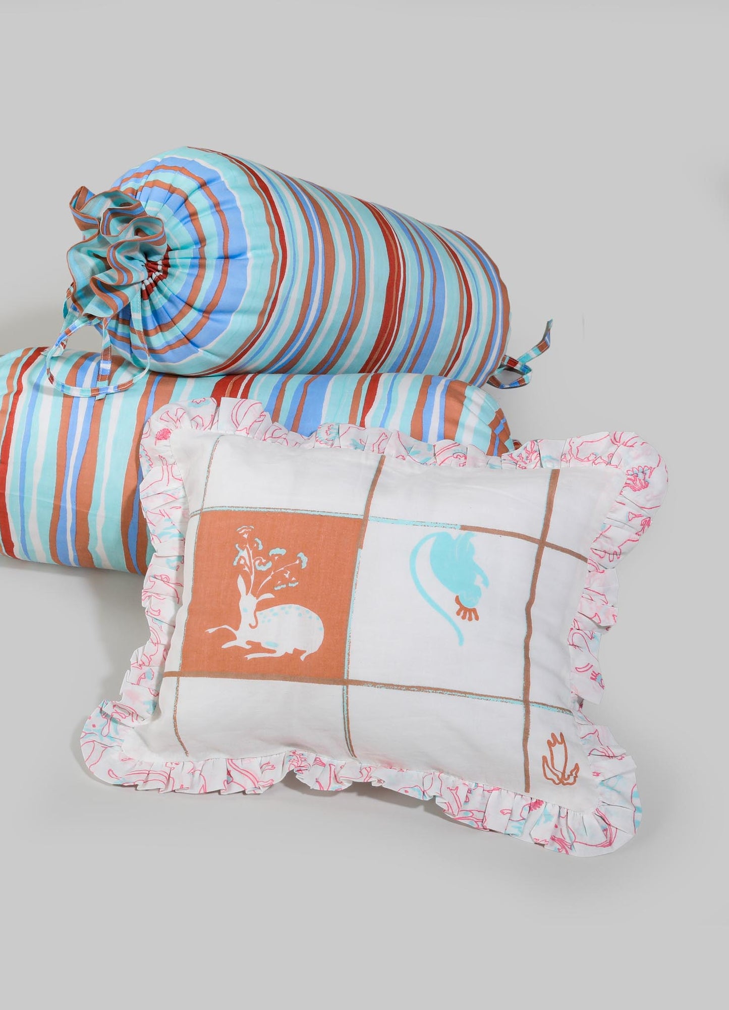 Striped fabric cushions with ruffled edges in shades of blue, orange, and white, featuring printed animal motifs of a rabbit and a bird on a patchwork design. The materials appear to be soft cotton or linen, and the style is casual and decorative.