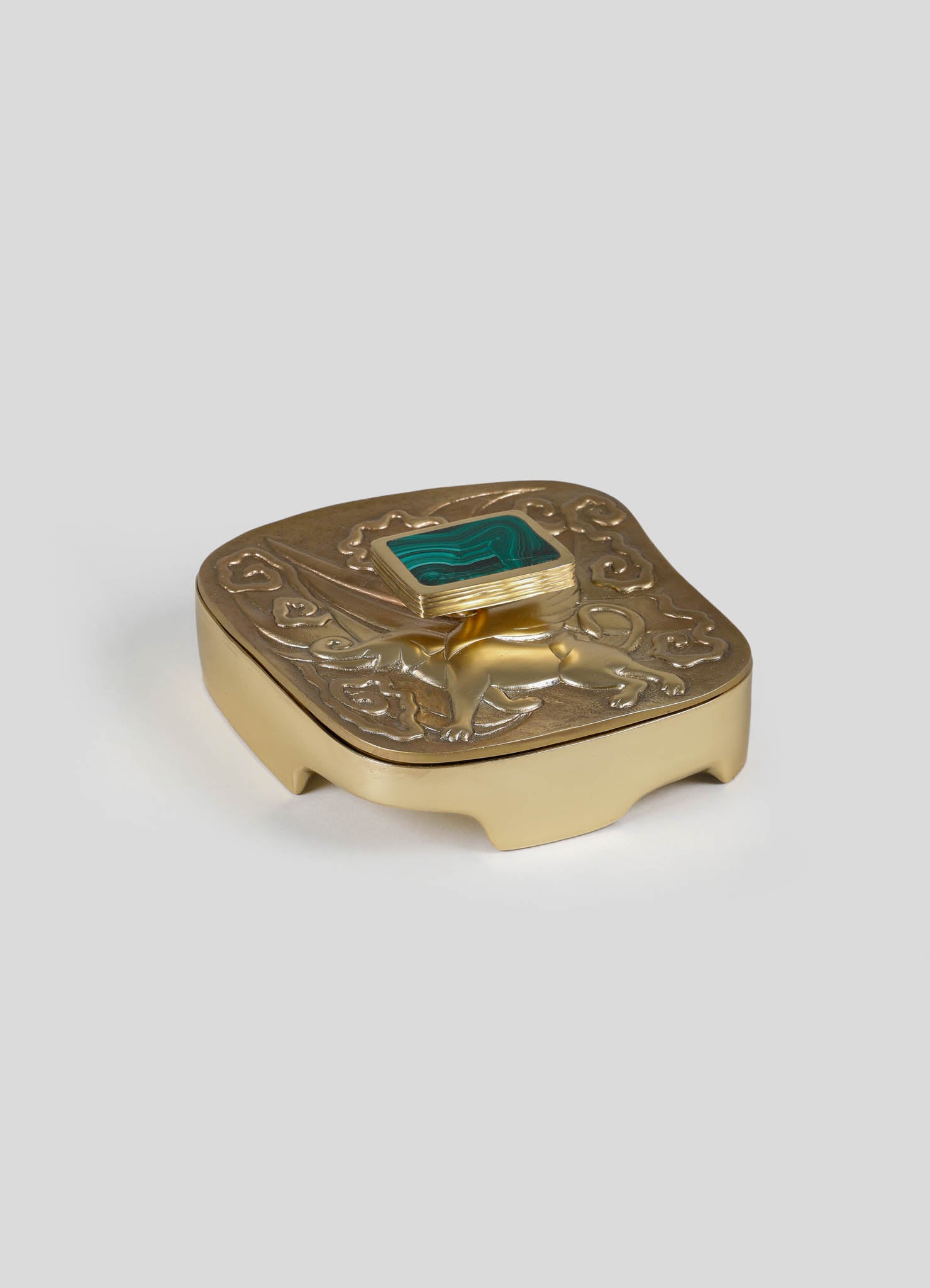 A decorative jewelry box with a gold-toned finish, featuring ornate embossed motifs on the lid and a square turquoise stone in a raised setting. The box has curved legs and a vintage-inspired design.