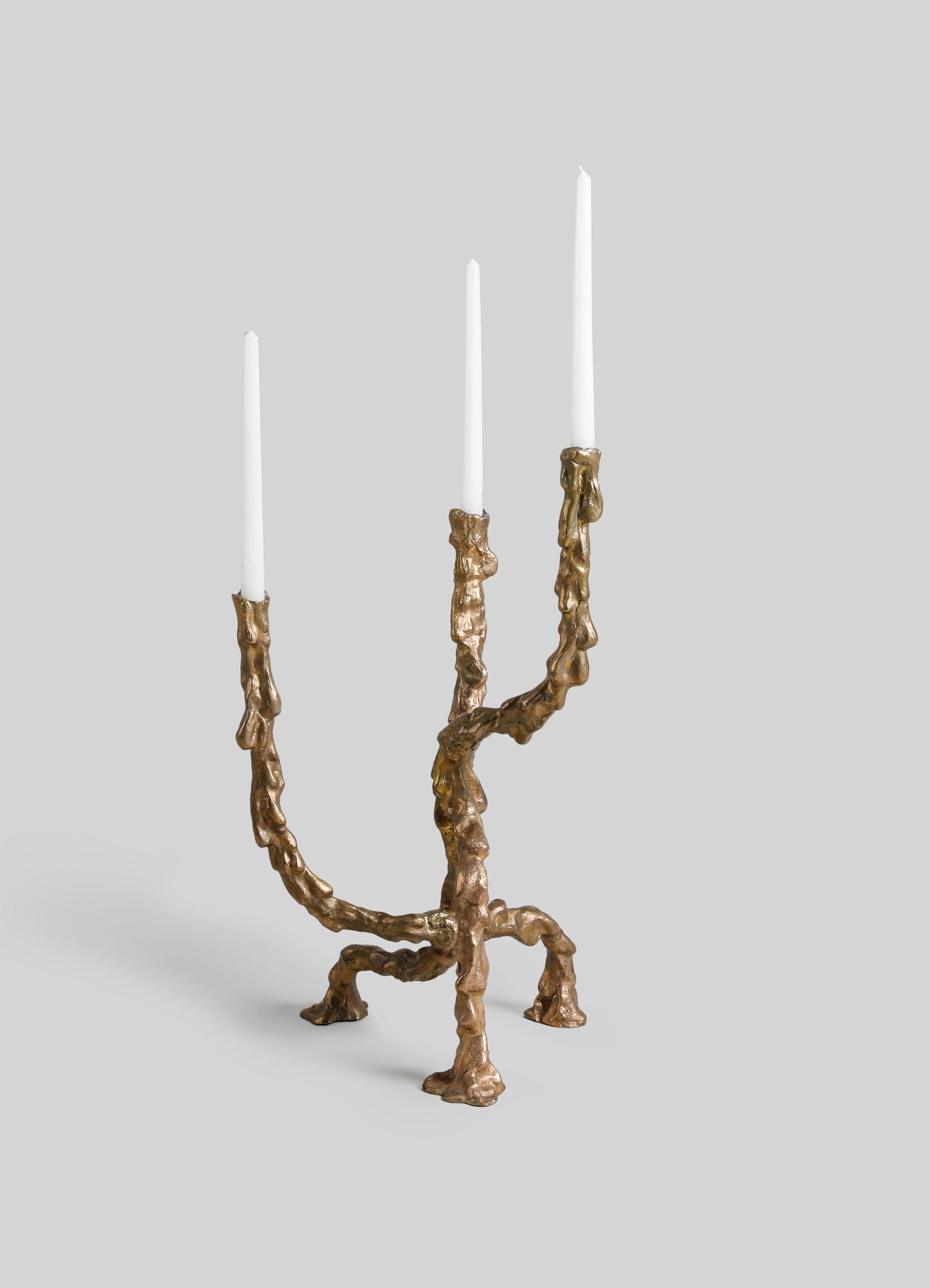 A bronze candle holder with an organic, textured design resembling melted or flowing forms, featuring three tapered white candles.