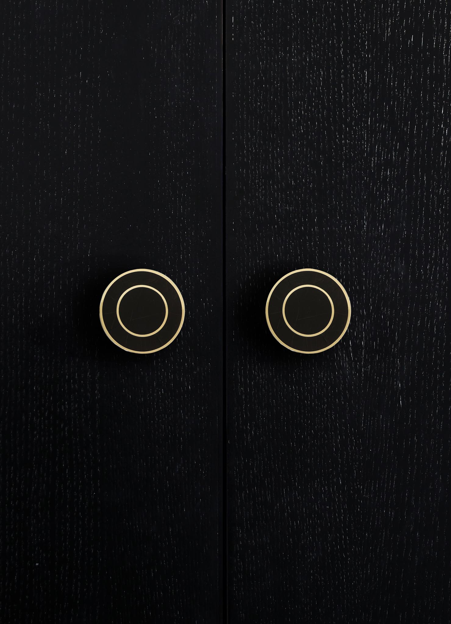 Black wooden cabinet doors with a textured finish, featuring two round brass handles with concentric circle design.