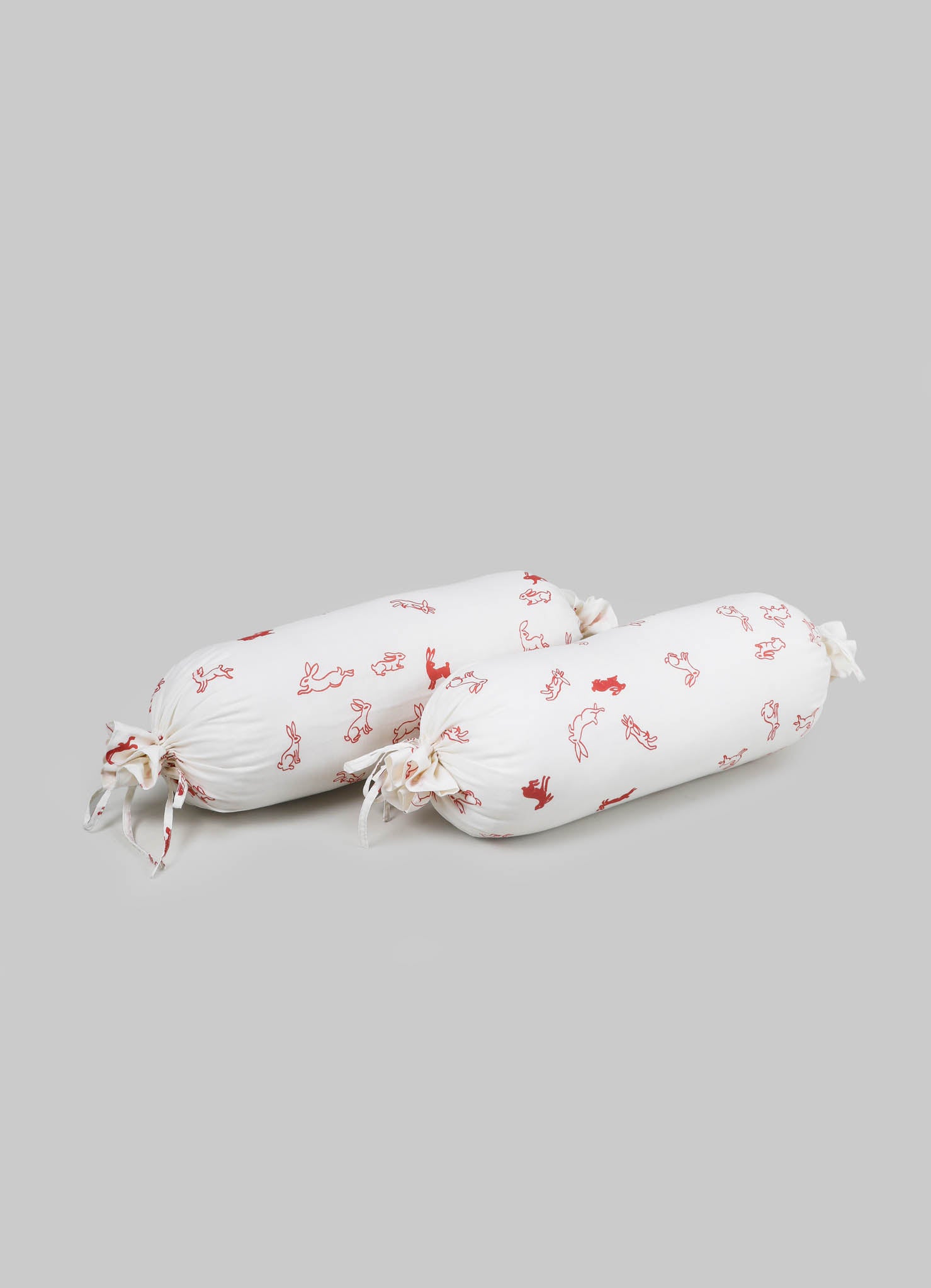 Cotton bolster pillow with a white background and red line-drawn animal motifs, featuring tied fabric ends for decorative detail.