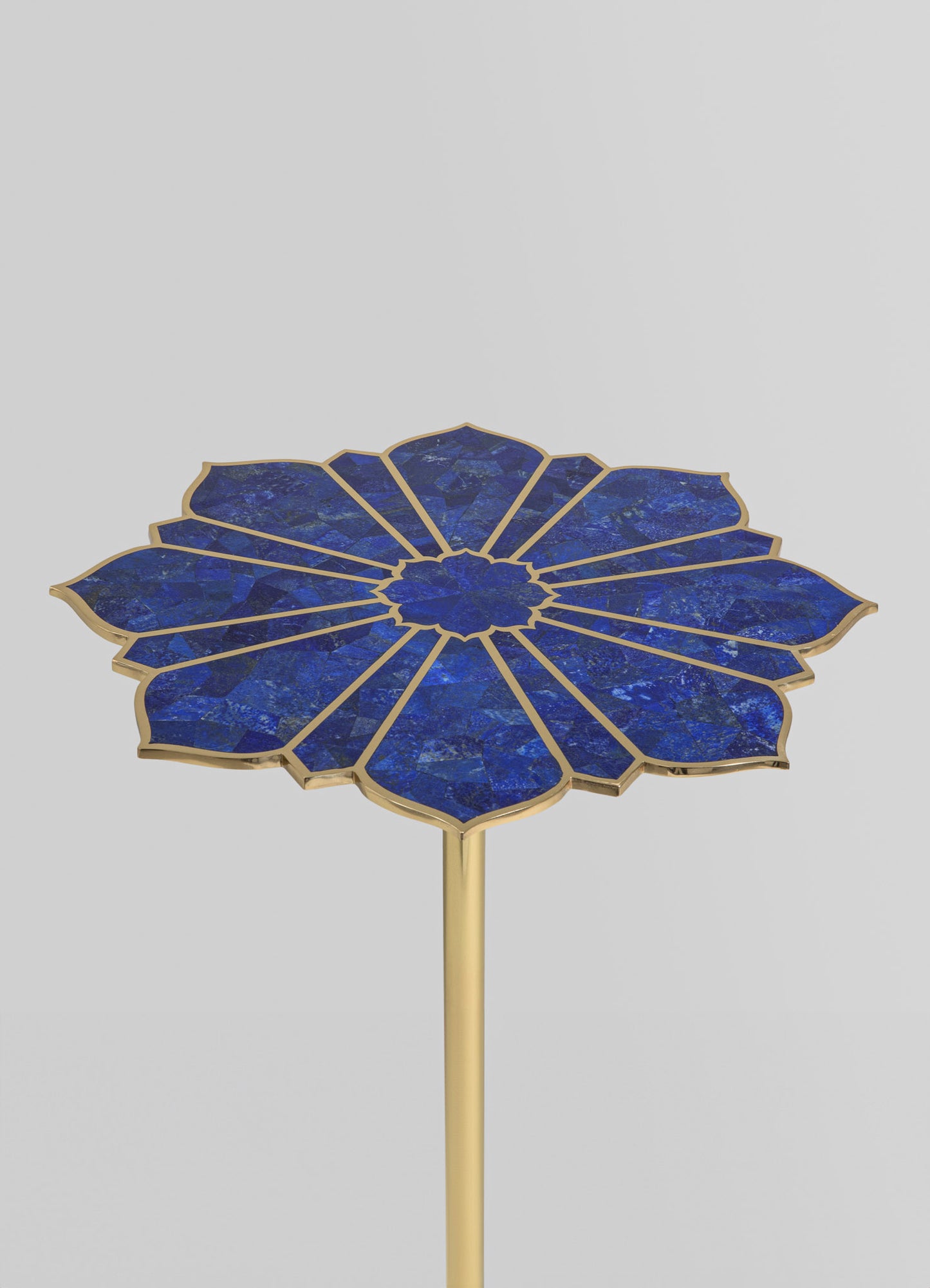 A side table with a floral-shaped top made of blue lapis lazuli inlay, outlined with a gold metallic frame and supported by a slender gold metal stem.