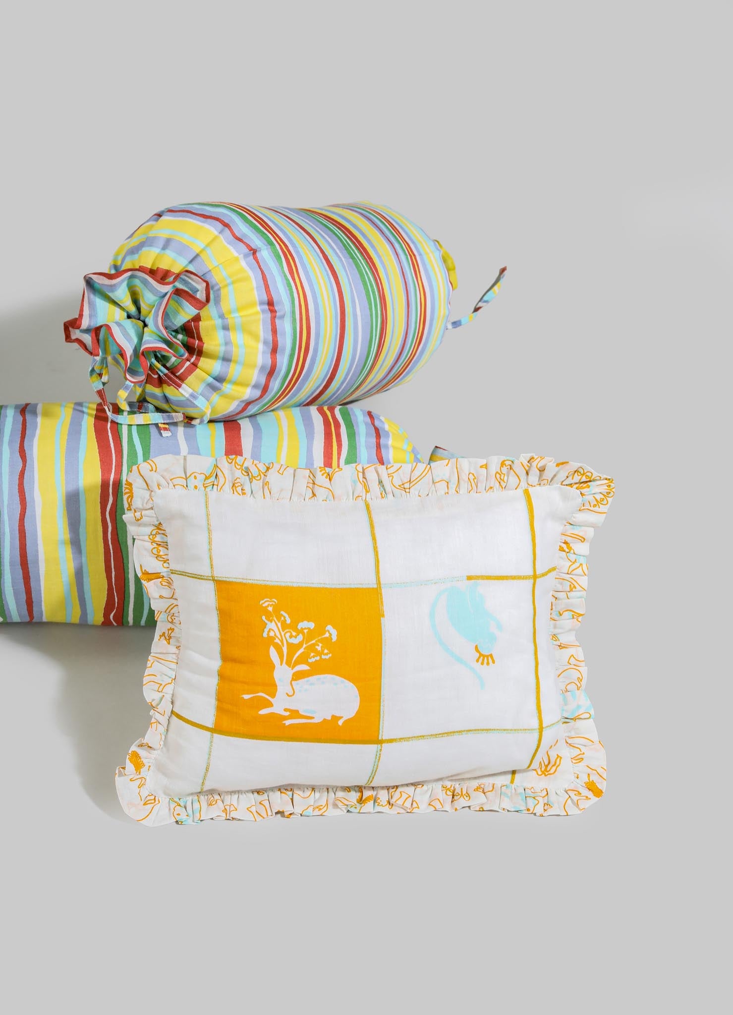 Colorful striped fabric cushions and a matching roll-up bolster pillow made from lightweight cotton, featuring vibrant rainbow hues and ruffled edges with decorative stitching.