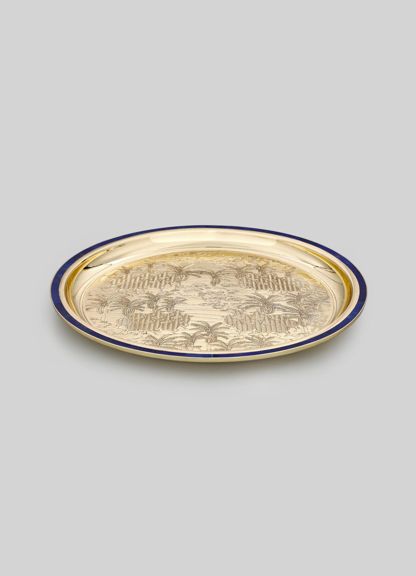A decorative metal tray with a gold-toned surface and a dark blue rim, featuring an engraved tropical landscape motif with palm trees.
