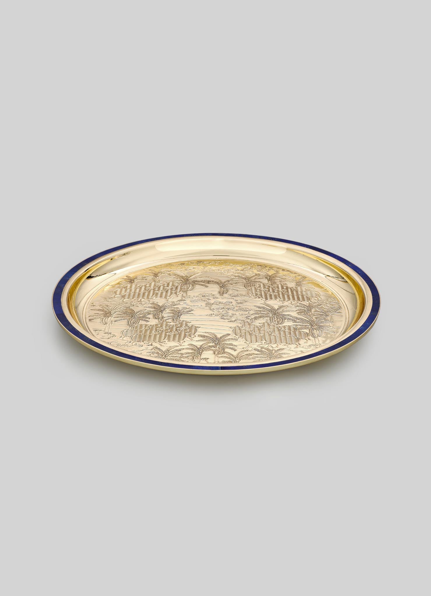 A decorative metal tray with a gold-toned surface and a dark blue rim, featuring an engraved tropical landscape motif with palm trees.