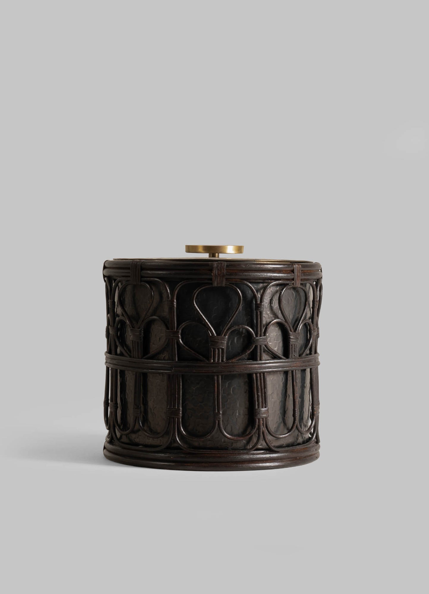 The VIYA Manipur Ice Bucket Large is a round, dark wooden container with intricate carvings and a flat, hand-beaten brass knob on top, displayed against a plain light gray background.