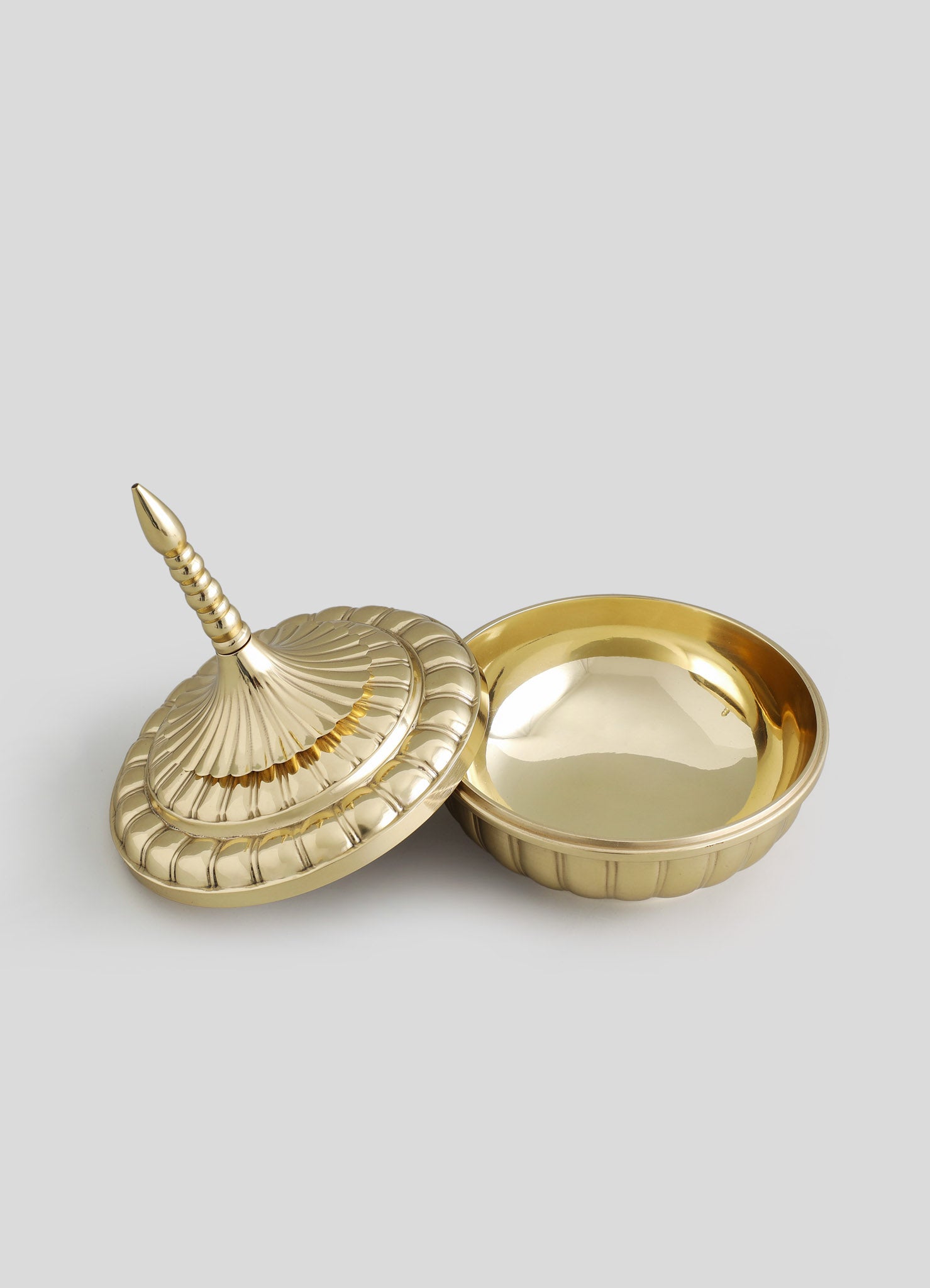 A decorative brass box with a removable lid featuring a pointed finial, with a scalloped edge design, and a matching interior tray. The metal has a polished, shiny finish.