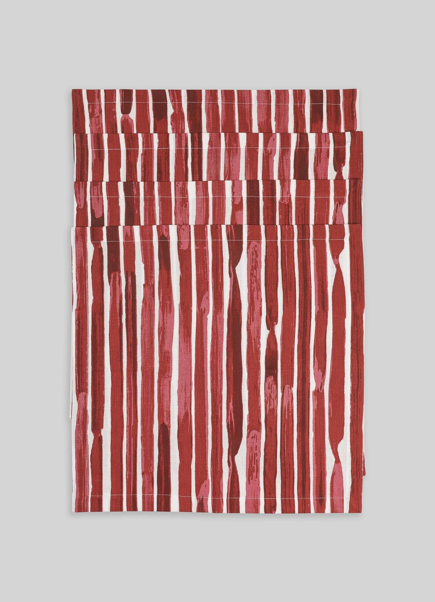 A set of fabric napkins featuring a vertical stripe pattern in shades of red and pink on a white background. The material appears to be linen or cotton with a textured, handcrafted look.