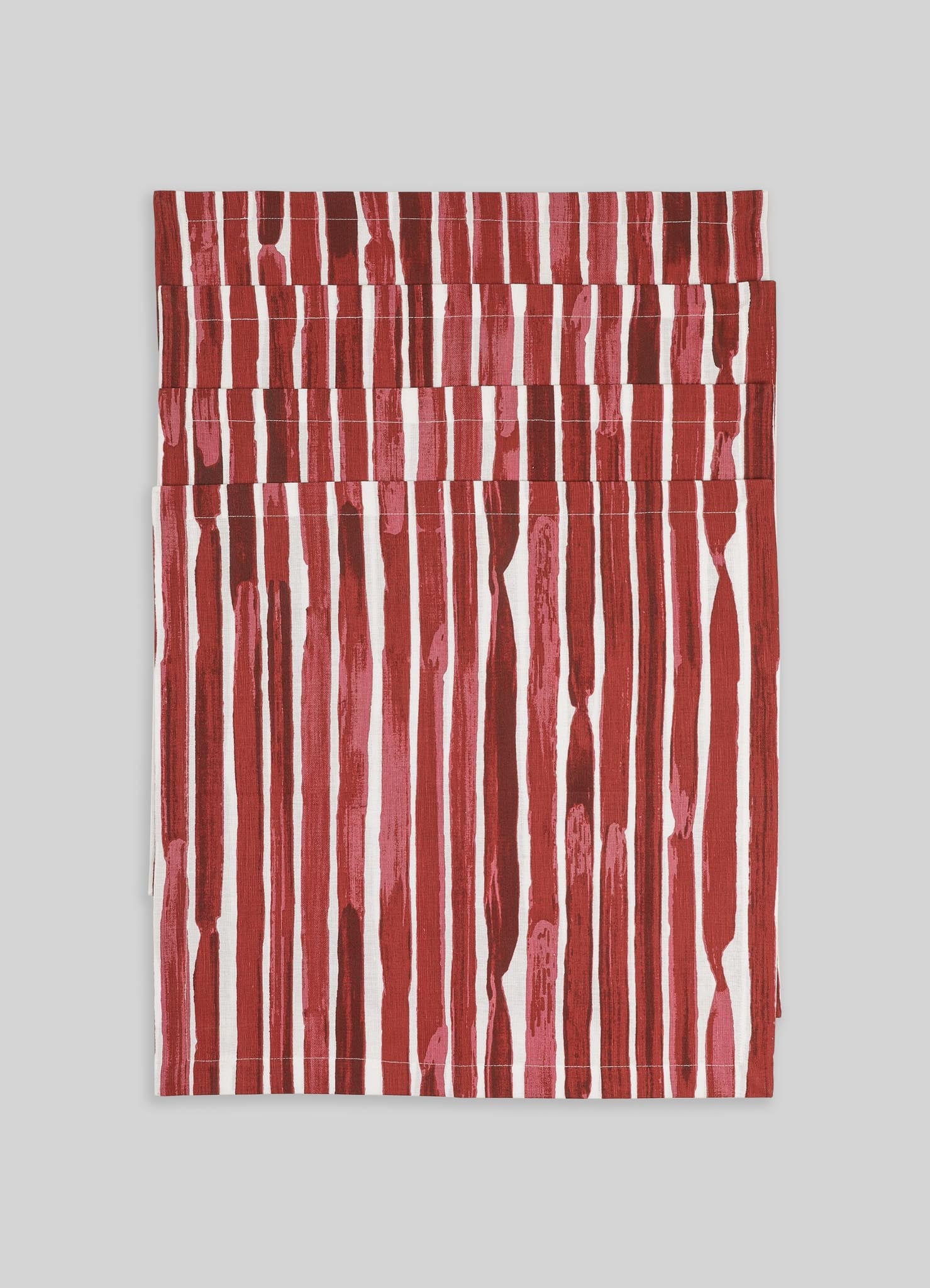 A set of fabric napkins featuring a vertical stripe pattern in shades of red and pink on a white background. The material appears to be linen or cotton with a textured, handcrafted look.