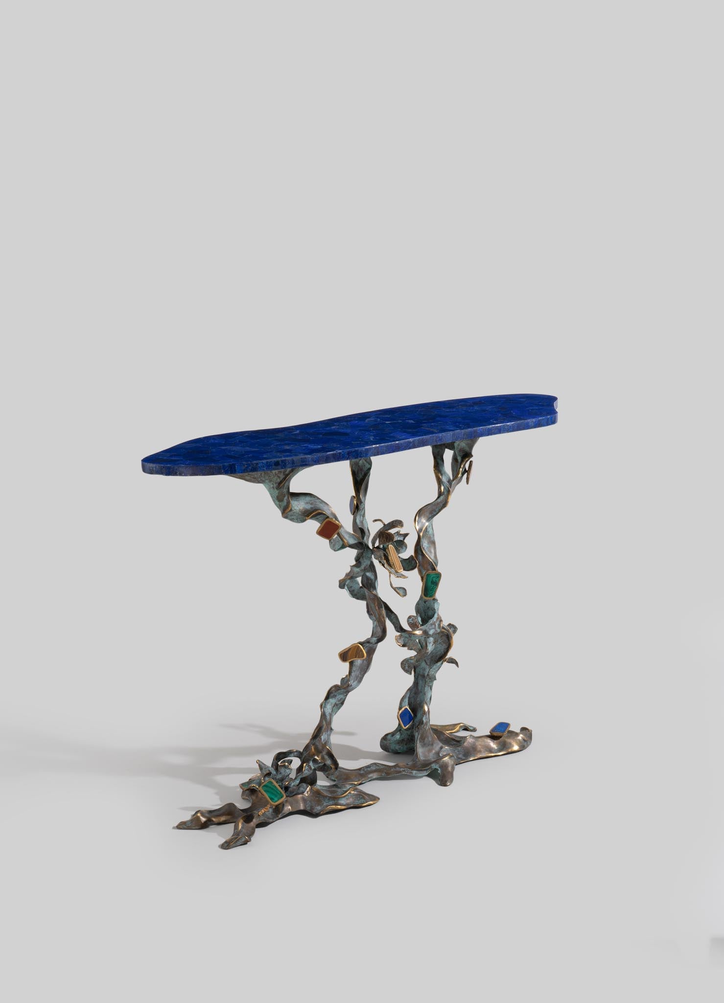 A decorative side table with a tabletop in deep blue lapis lazuli and a sculptural metal base featuring an abstract, organic design with colorful gemstone accents.