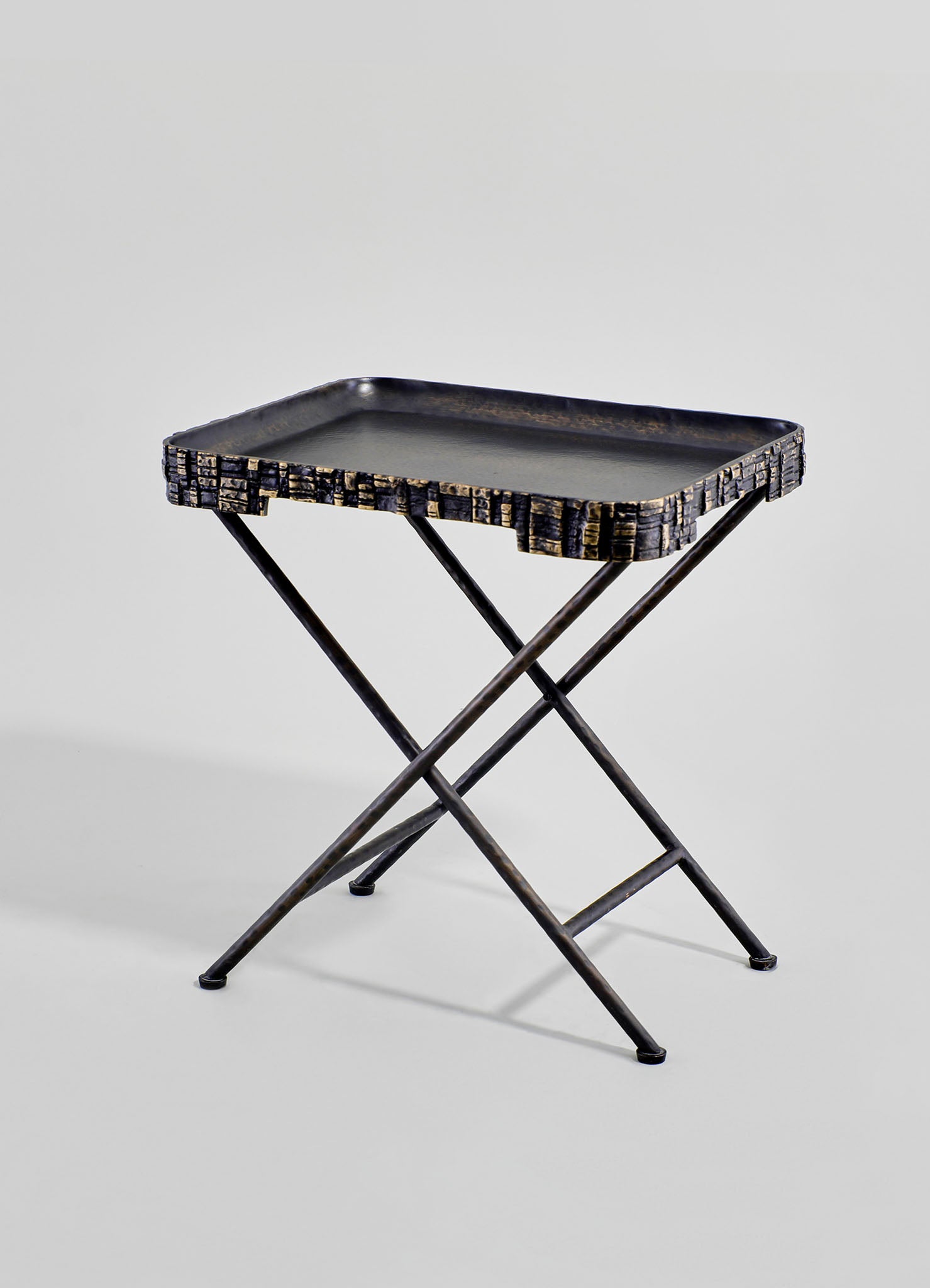 A black wooden tray with a textured, carved rim on a black X-shaped wooden stand. The tray has a rectangular shape with rounded edges and a smooth, flat surface.