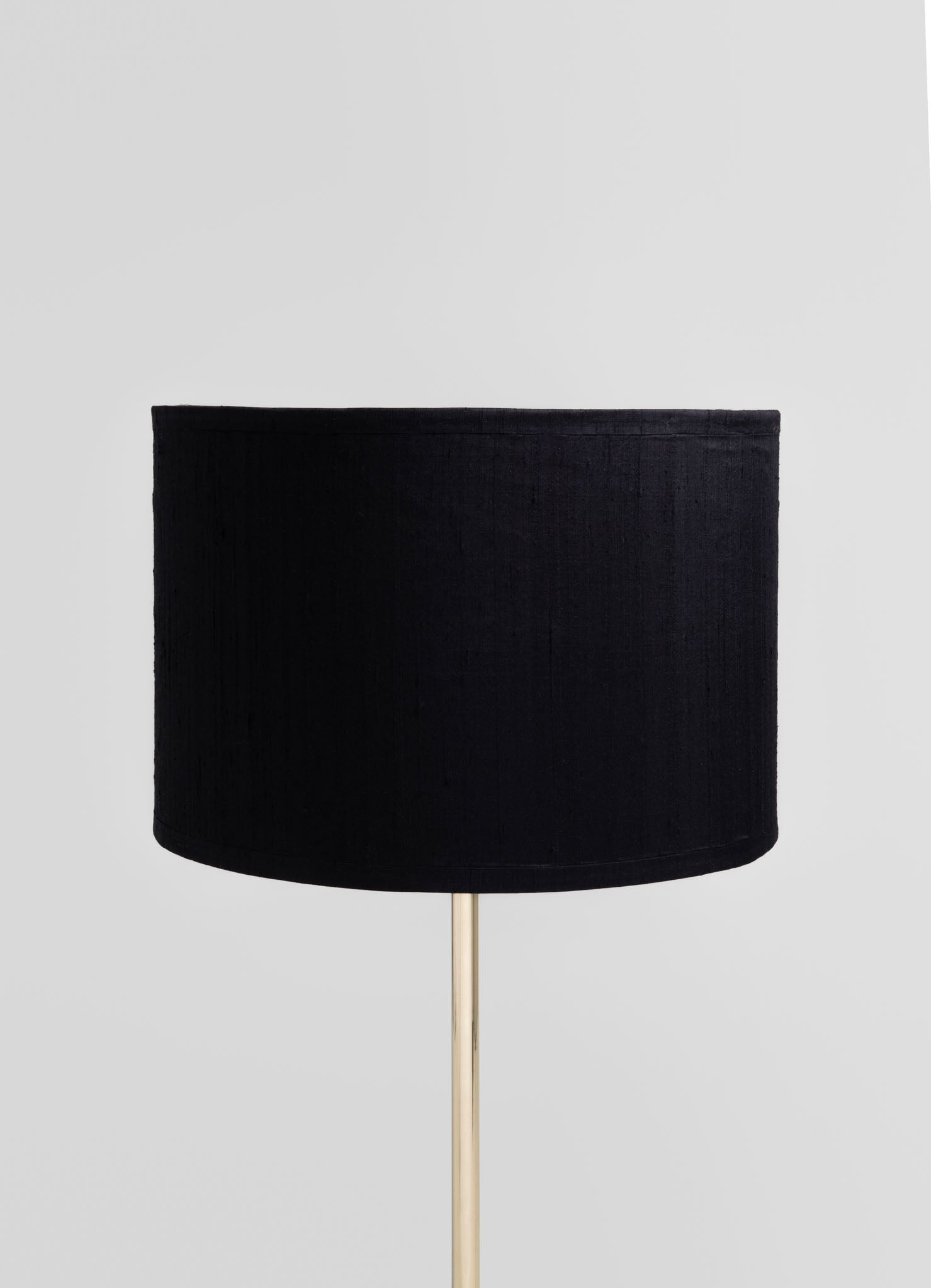 A floor lamp with a cylindrical black fabric lampshade and a slender metallic gold stand, creating a contemporary and minimalist style.