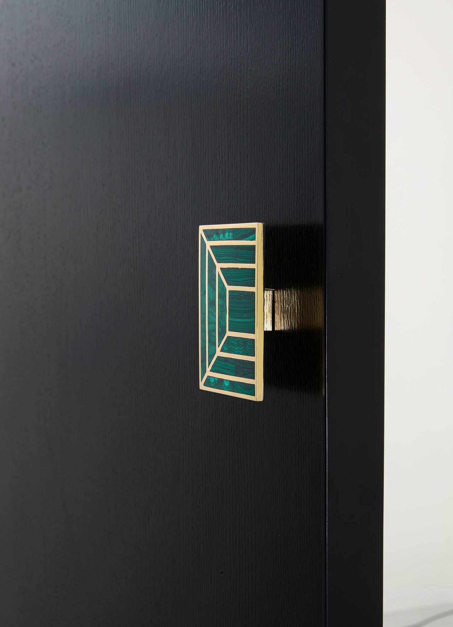 Close-up of a black wooden furniture piece with a decorative rectangular handle featuring an geometric pattern in green and gold tones. The style appears modern and sleek, emphasizing minimalism and clean lines.