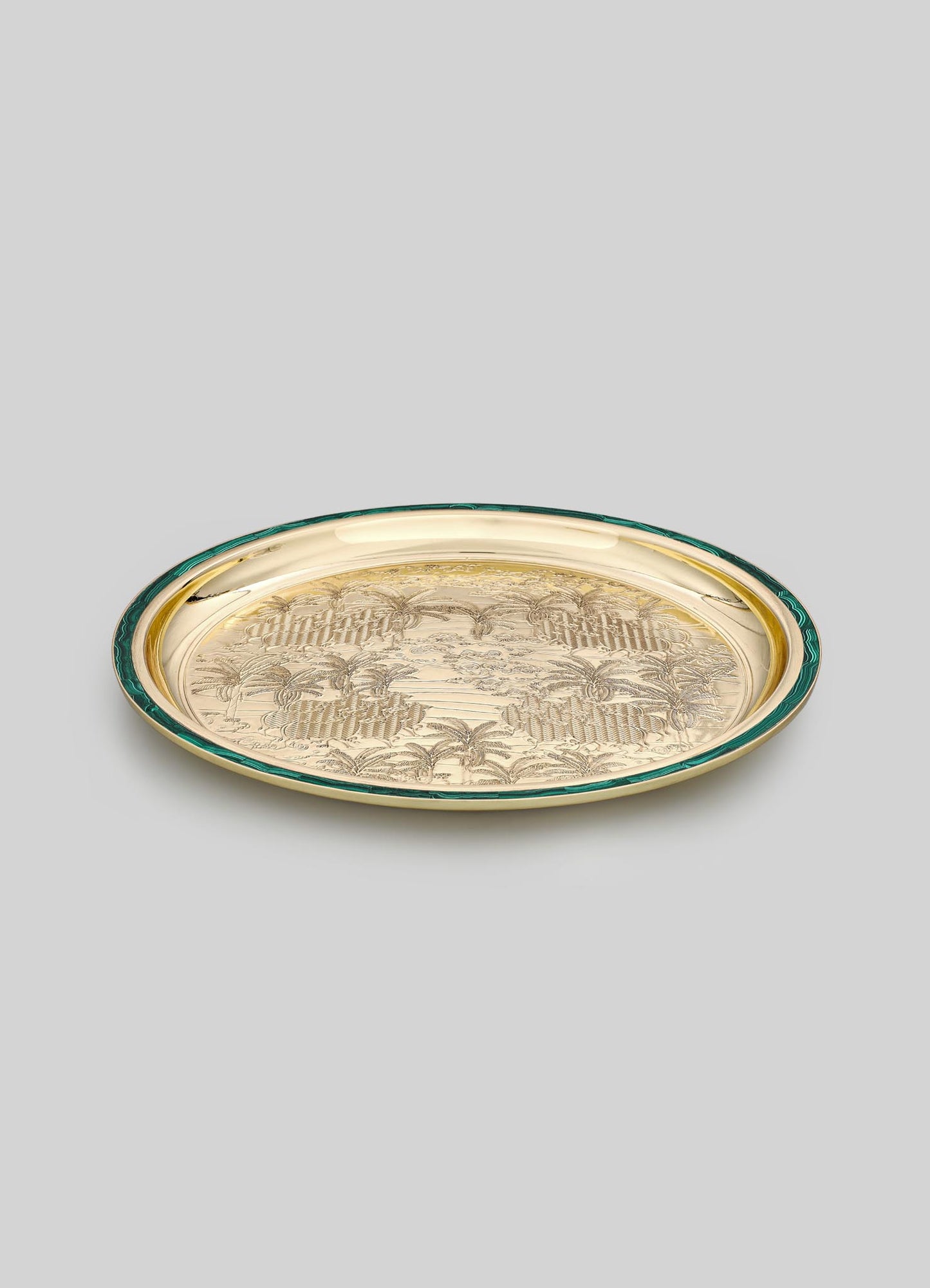 A decorative tray with a gold-tone metal surface engraved with a floral and palm motif, bordered by a dark green edge. The tray has an oval shape and a polished finish.