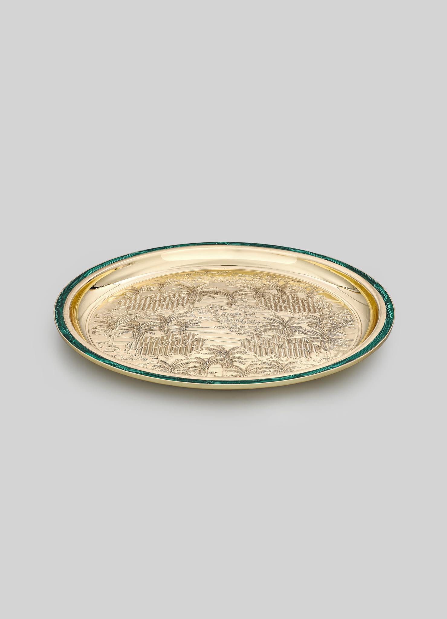 A decorative tray with a gold-tone metal surface engraved with a floral and palm motif, bordered by a dark green edge. The tray has an oval shape and a polished finish.