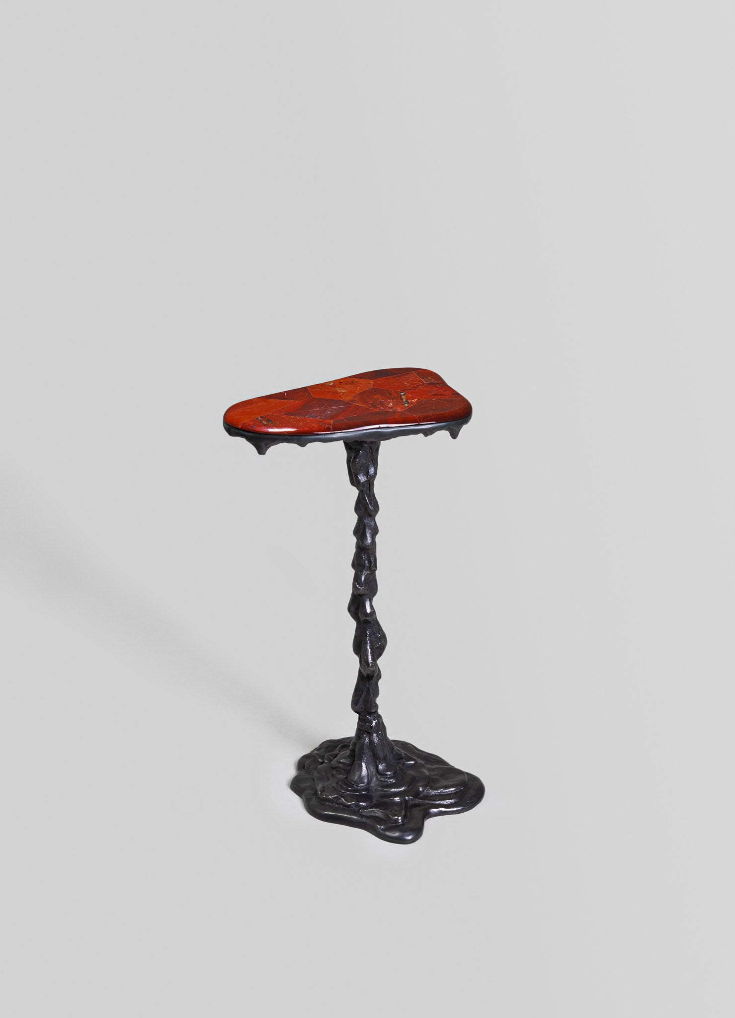 A small side table with a irregularly shaped red marble top and a sculptural black metal base with a textured, organic form.