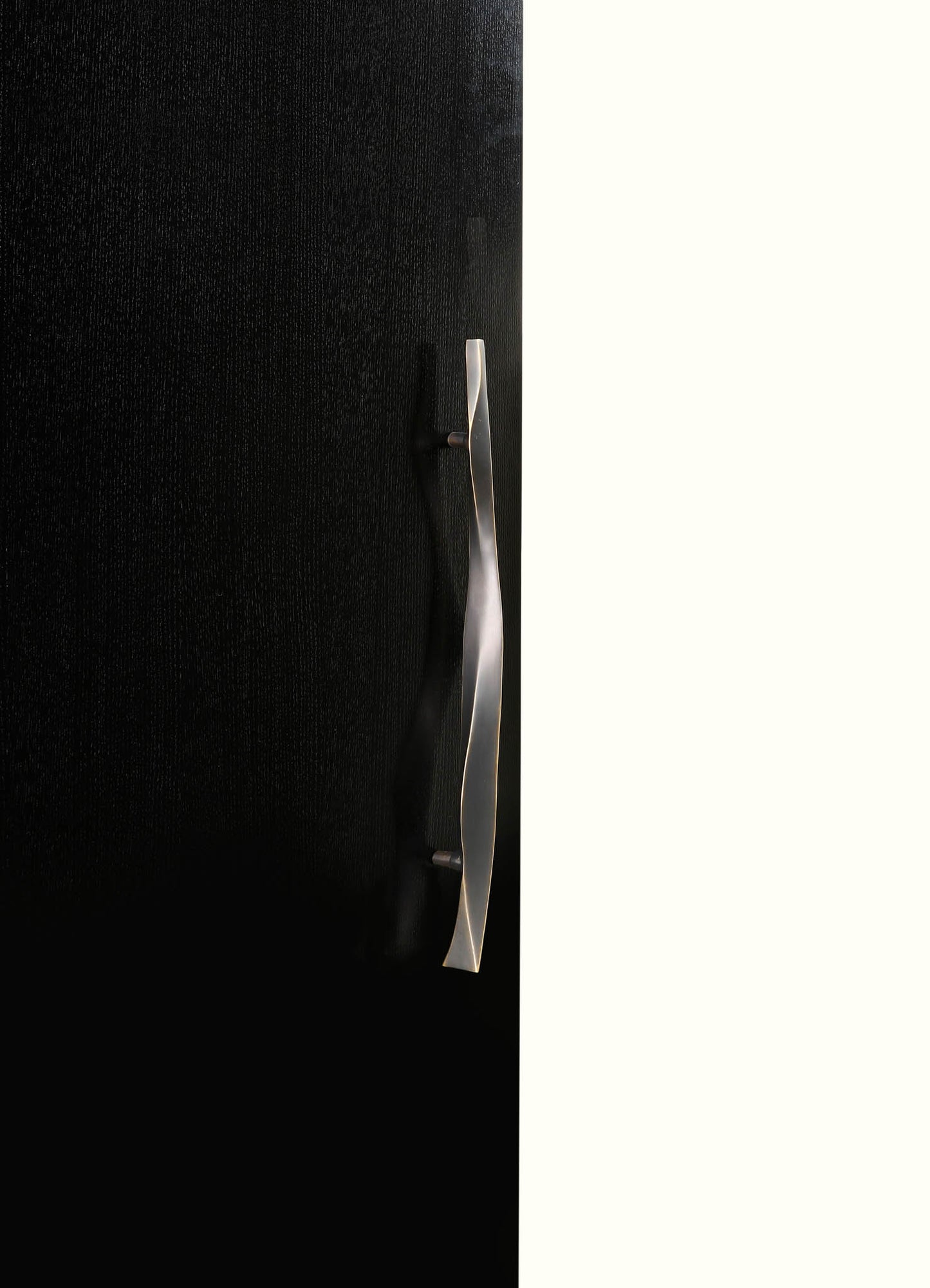 A black textured surface with a metallic silver handle or decorative element mounted vertically, contrasting with a white background. The design appears modern and minimalist, emphasizing sleek lines and materials.