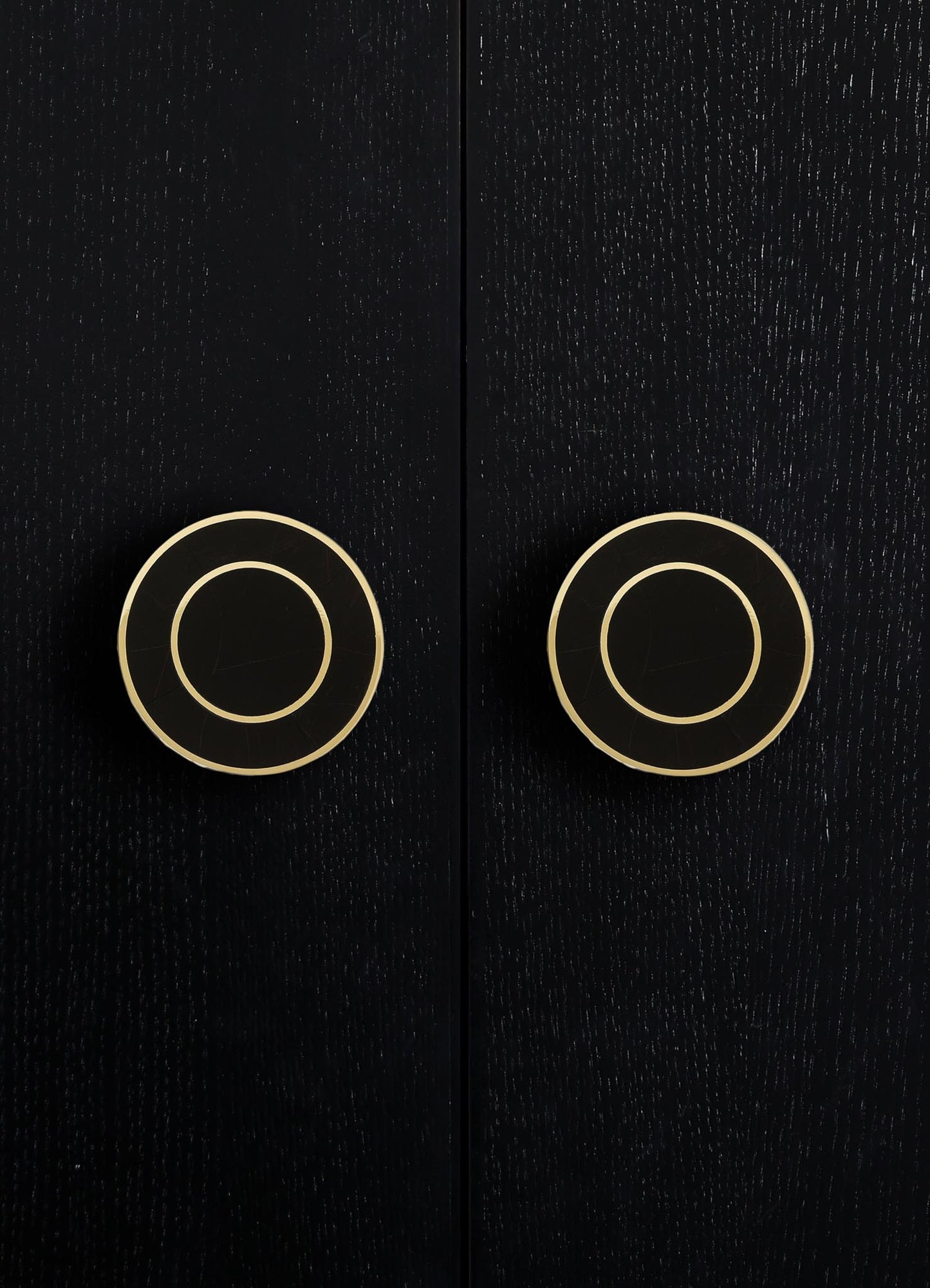 Close-up of a dark wooden surface with two gold-colored circular handles or knobs, featuring concentric circle patterns, on a black background.
