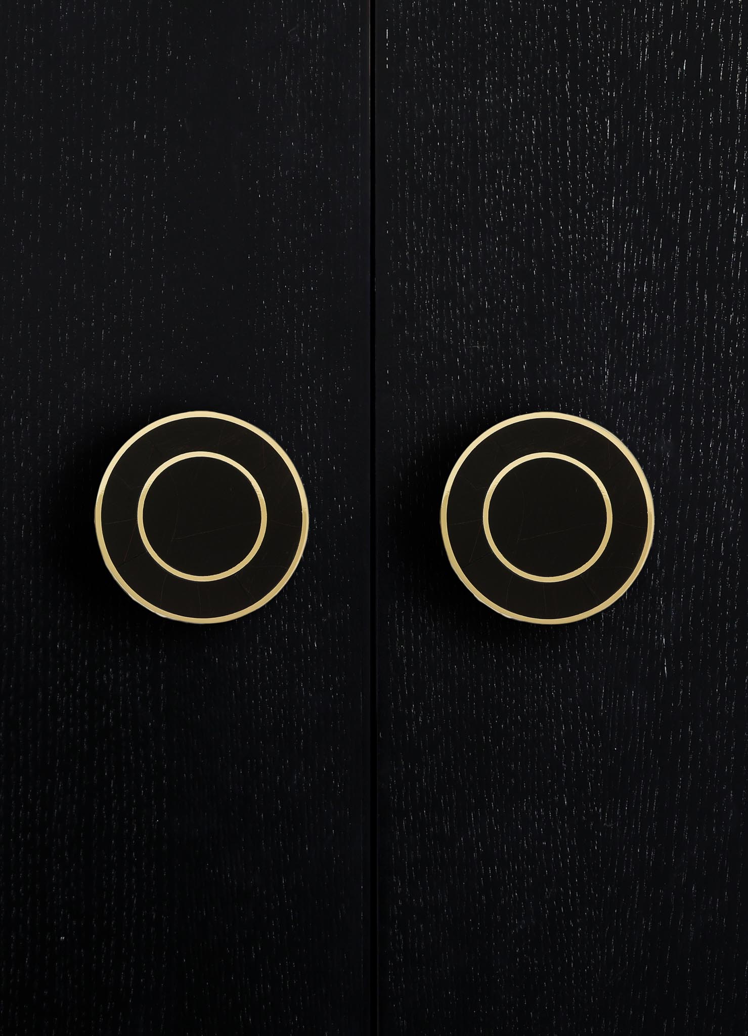 Close-up of a dark wooden surface with two gold-colored circular handles or knobs, featuring concentric circle patterns, on a black background.