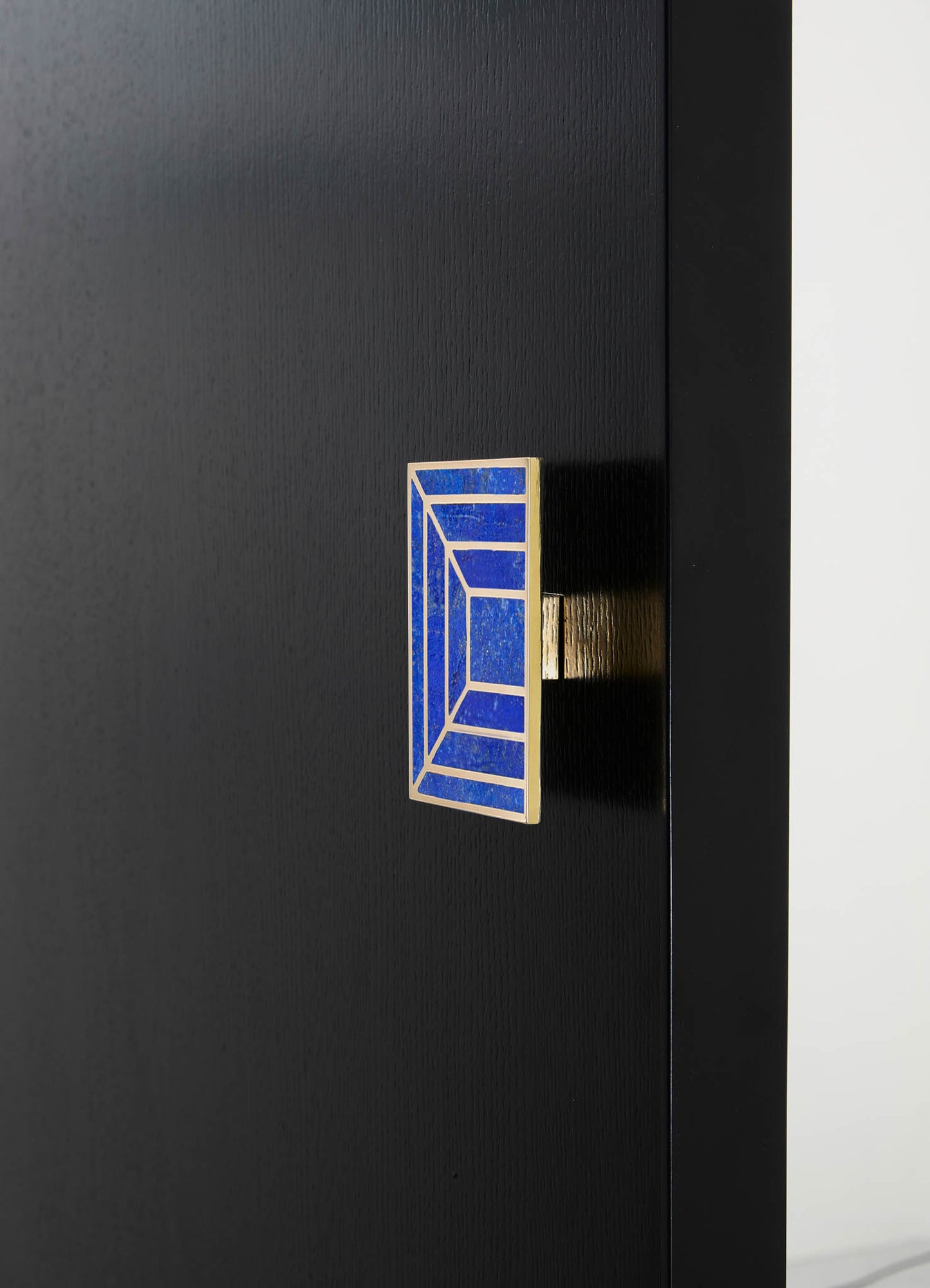 Close-up of a black wood cabinet with a geometric tile handle in blue and white with metallic accents, highlighting a modern, minimalist design.